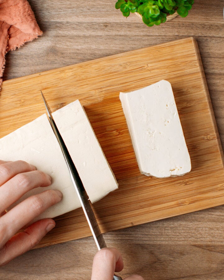 Chopping a block of tofu on a cutting board.