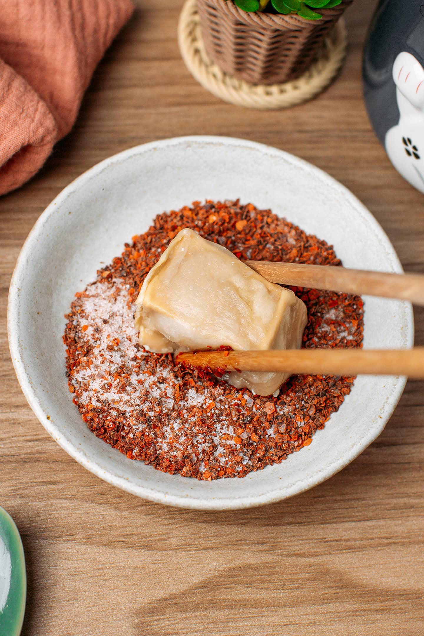 Coating a piece of stinky tofu with red pepper flakes in a small plate.