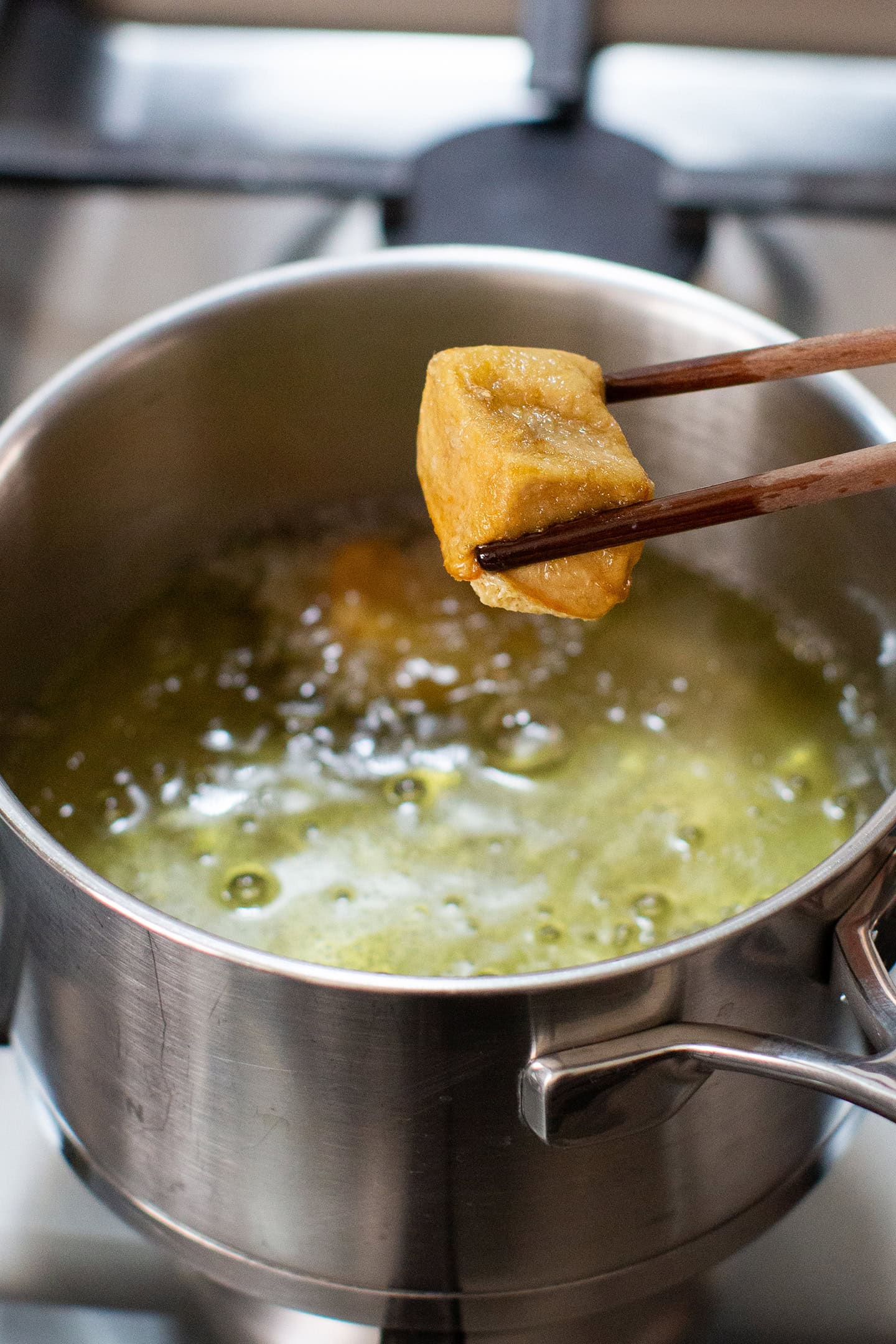 Holding a piece of fried tofu over a pot of oil.
