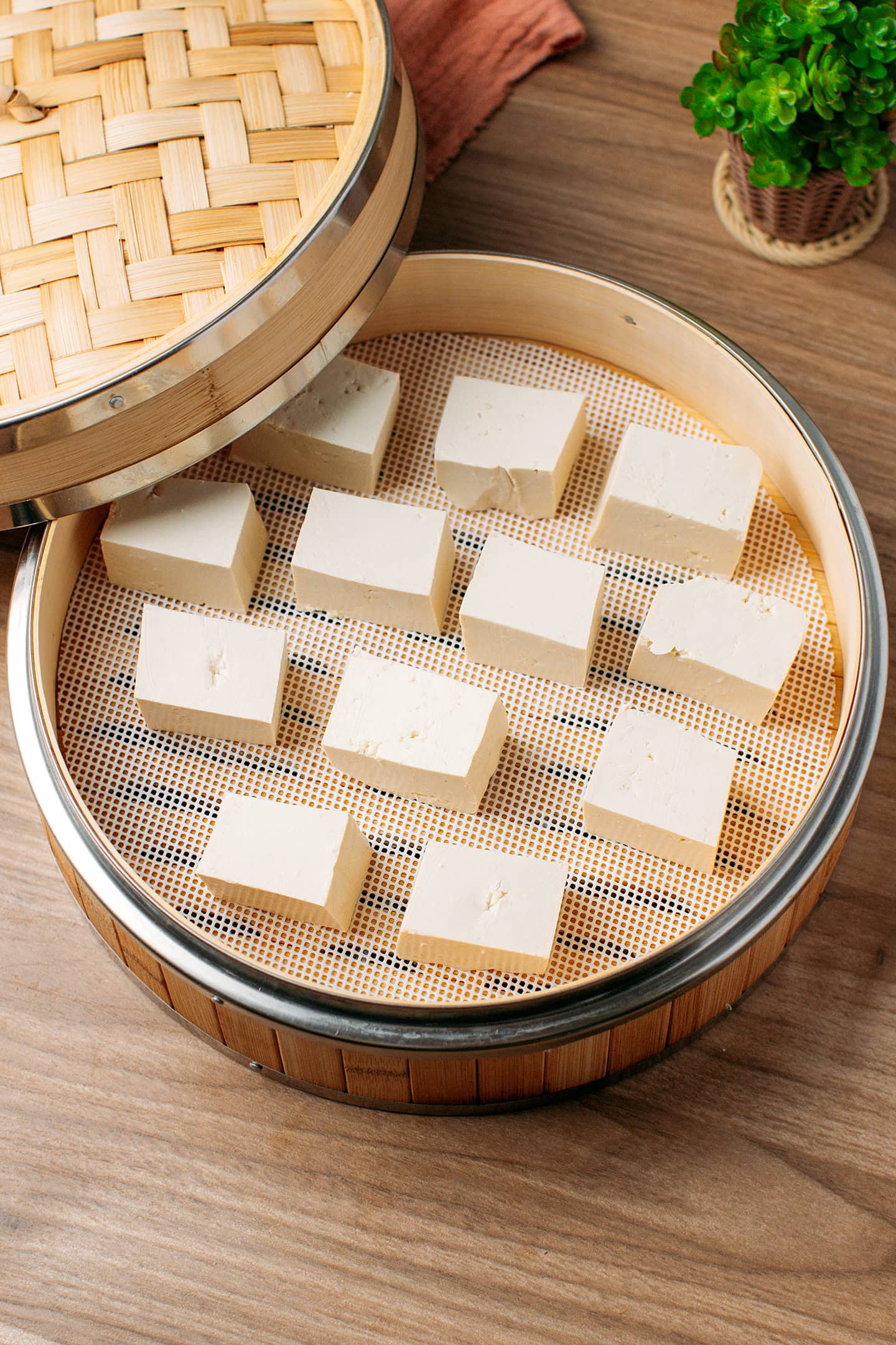 Twelve pieces of tofu inside a bamboo steamer basket.