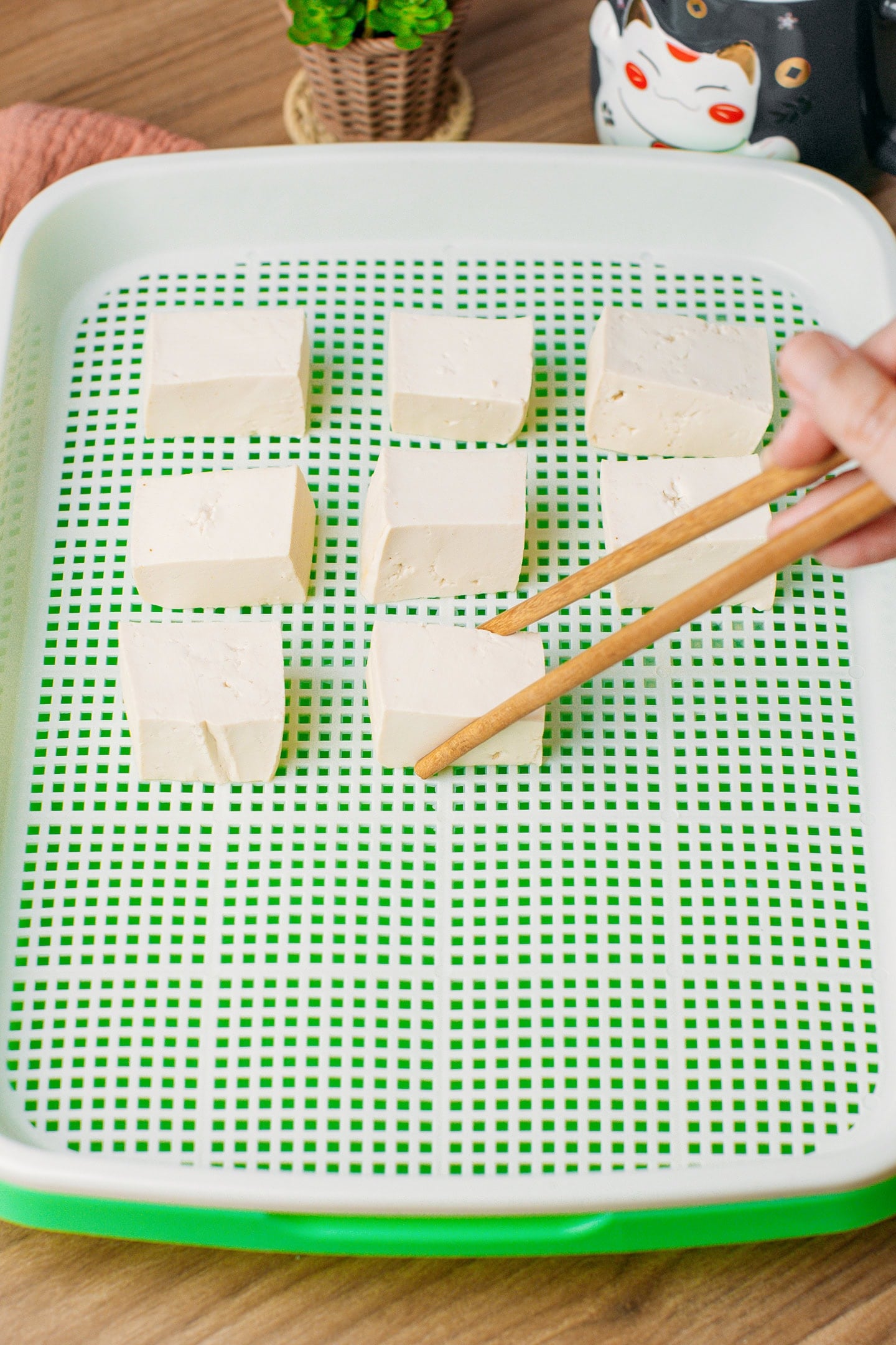 Using chopsticks to arrange tofu cubes inside a container.