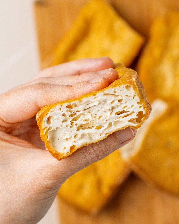 Holding a piece of sliced fried tofu revealing the white inside.