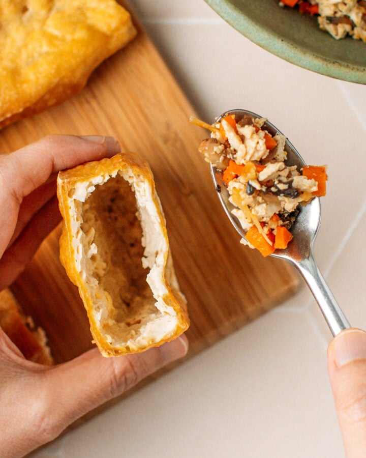Holding a spoonful of vegetable filling over a block of fried tofu.