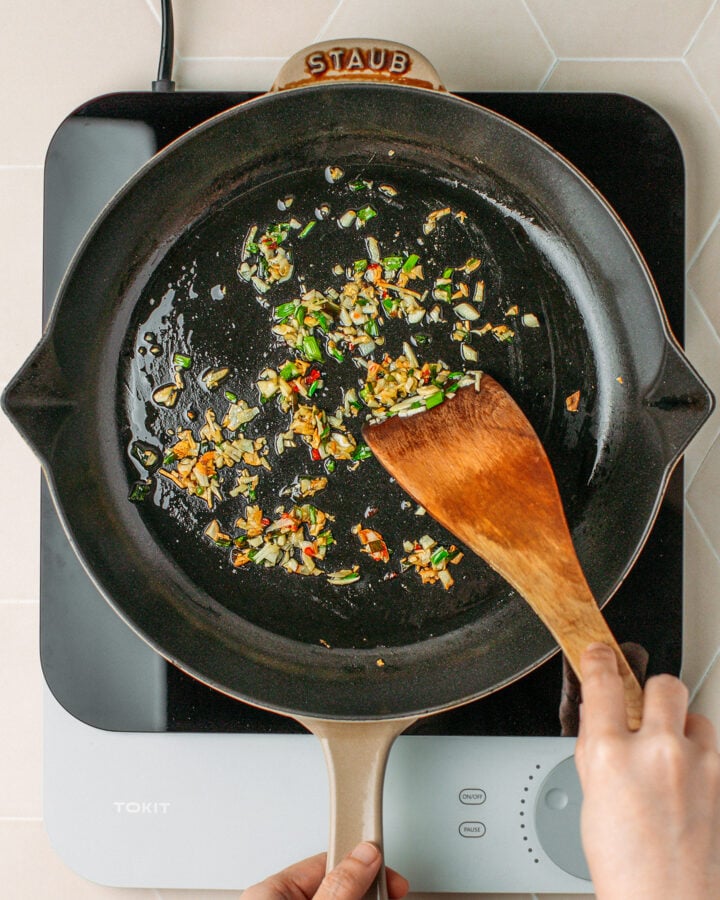 Sautéed garlic, green onions, and chili in a skillet.