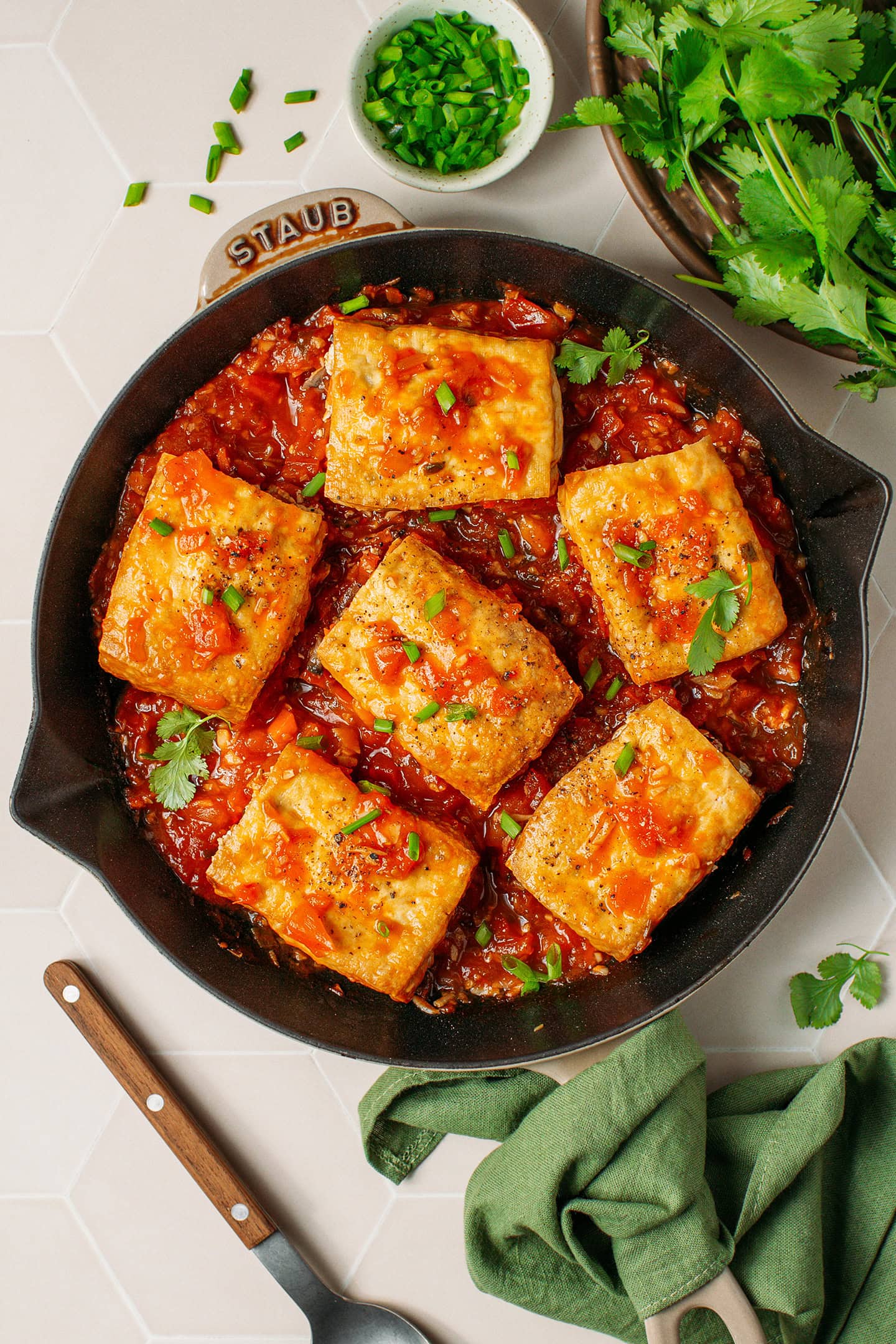 Six pieces of stuffed tofu in tomato sauce in a skillet.