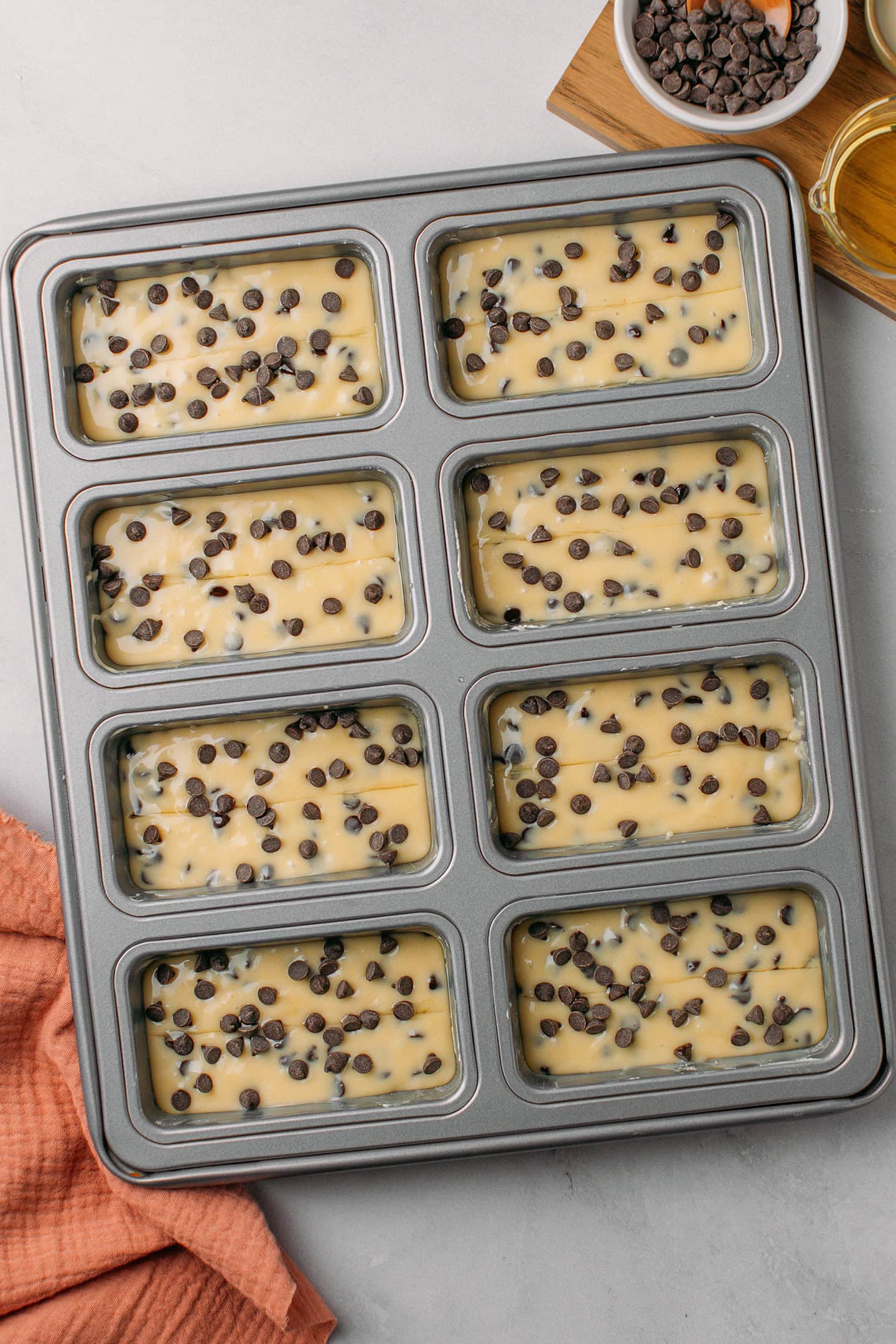 Mini loaf cake pan with 8 cavities filled with cake batter and topped with chocolate chips.