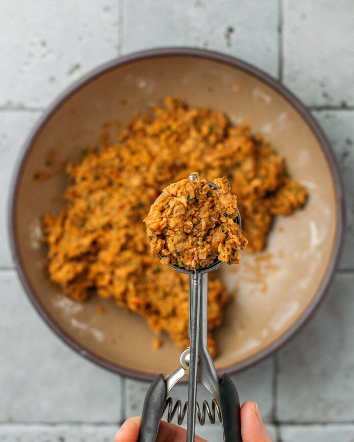 Holding a cookie scoop filled with meatball mixture.