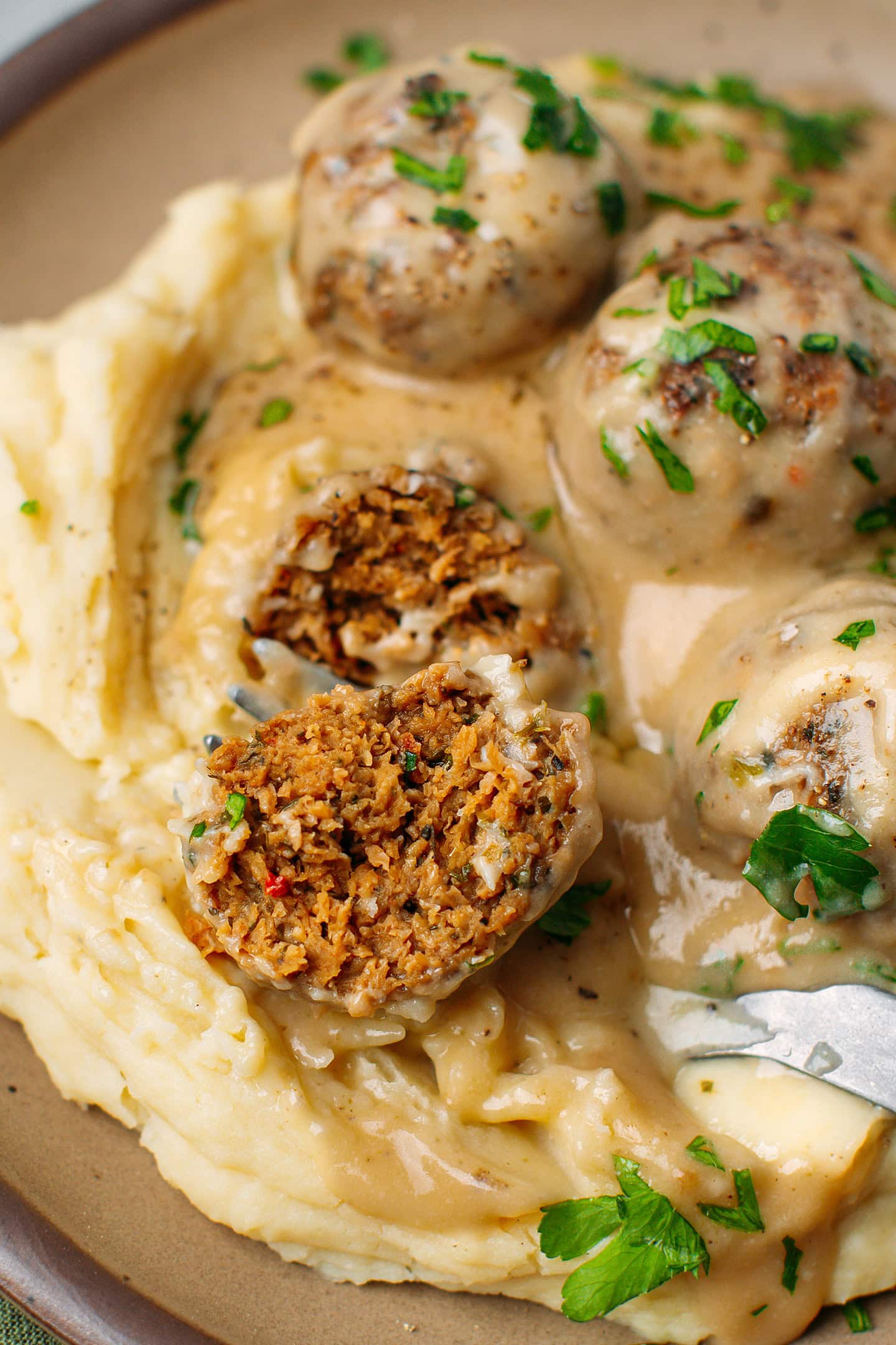 Close-up of a vegan meatballs sliced in half over mashed potatoes.