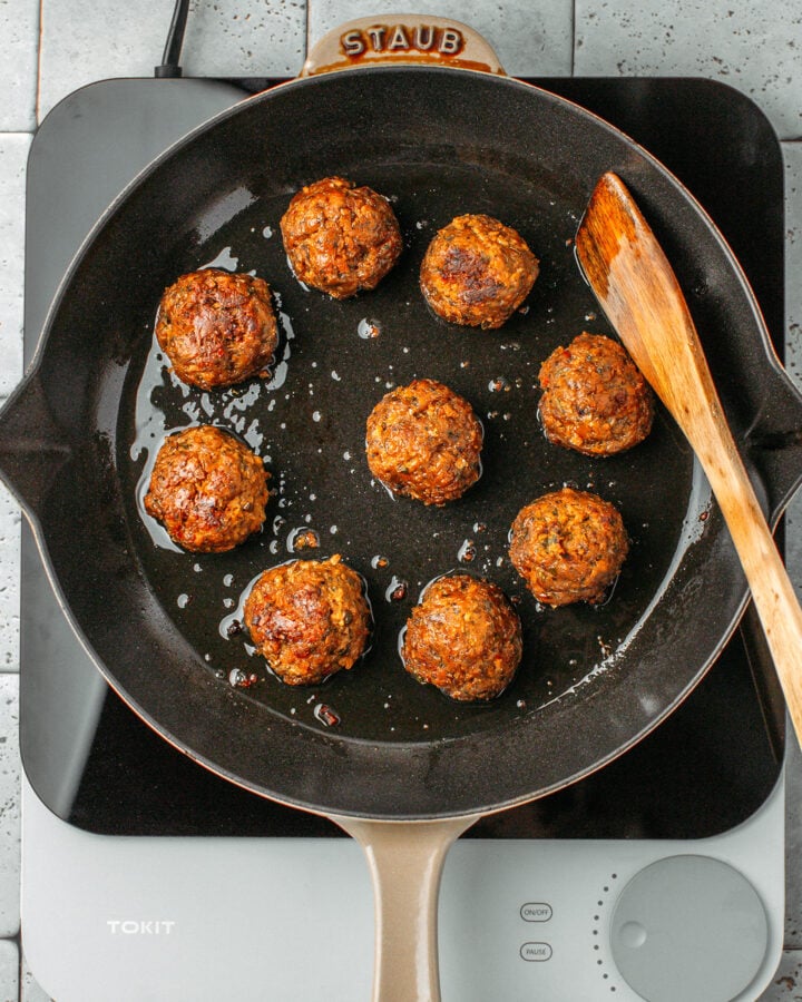 Nine saut&eacute;ed vegan meatballs in a skillet.
