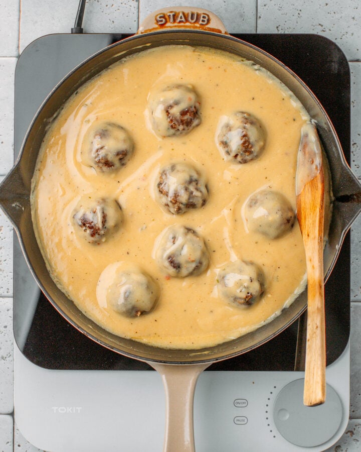 Nine vegan meatballs tossed with a creamy beige sauce in a skillet.