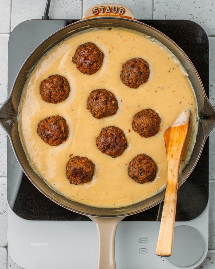 Nine vegan meatballs arranged in a beige sauce in a skillet.