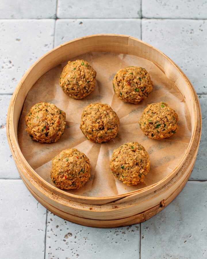 Seven meatballs in a bamboo basket steamer before steaming.