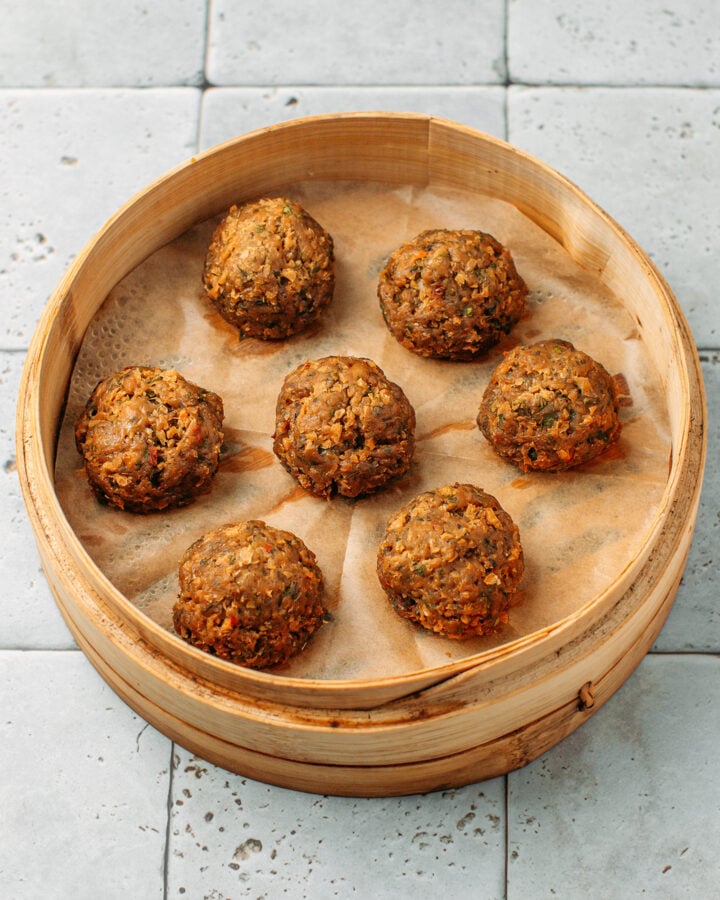 Seven meatballs in a bamboo basket steamer after steaming.