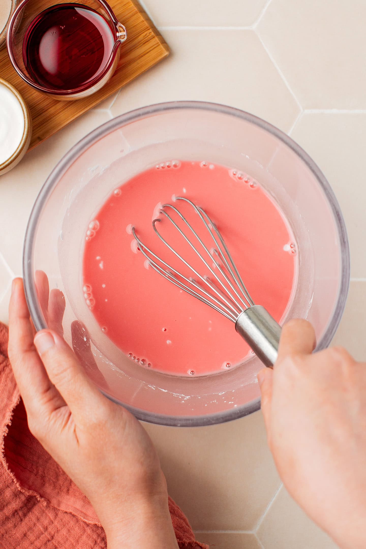 Whisking a pink batter in a glass bowl.
