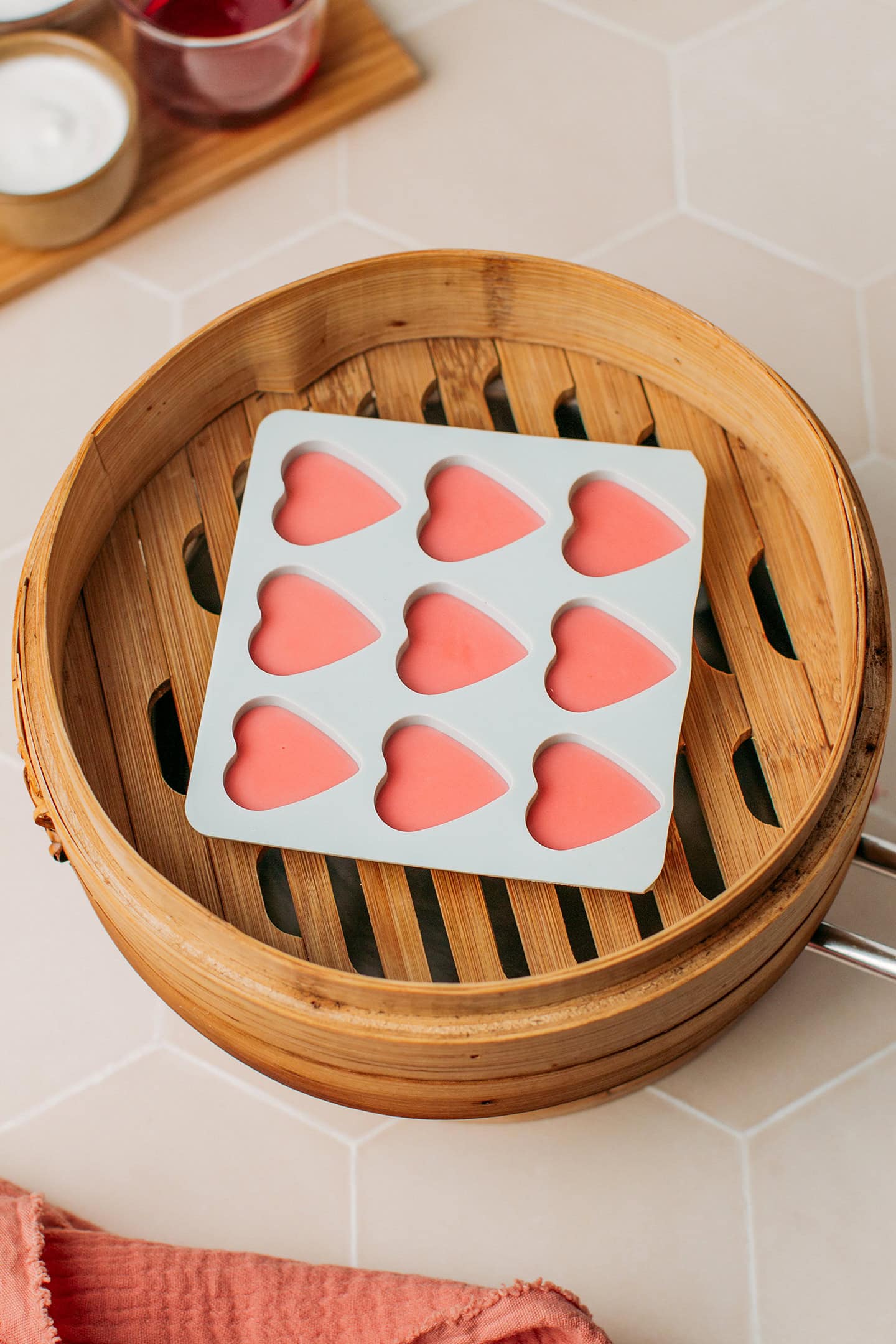 Heart-shaped silicone mold filled with a red batter in a bamboo basket steamer.