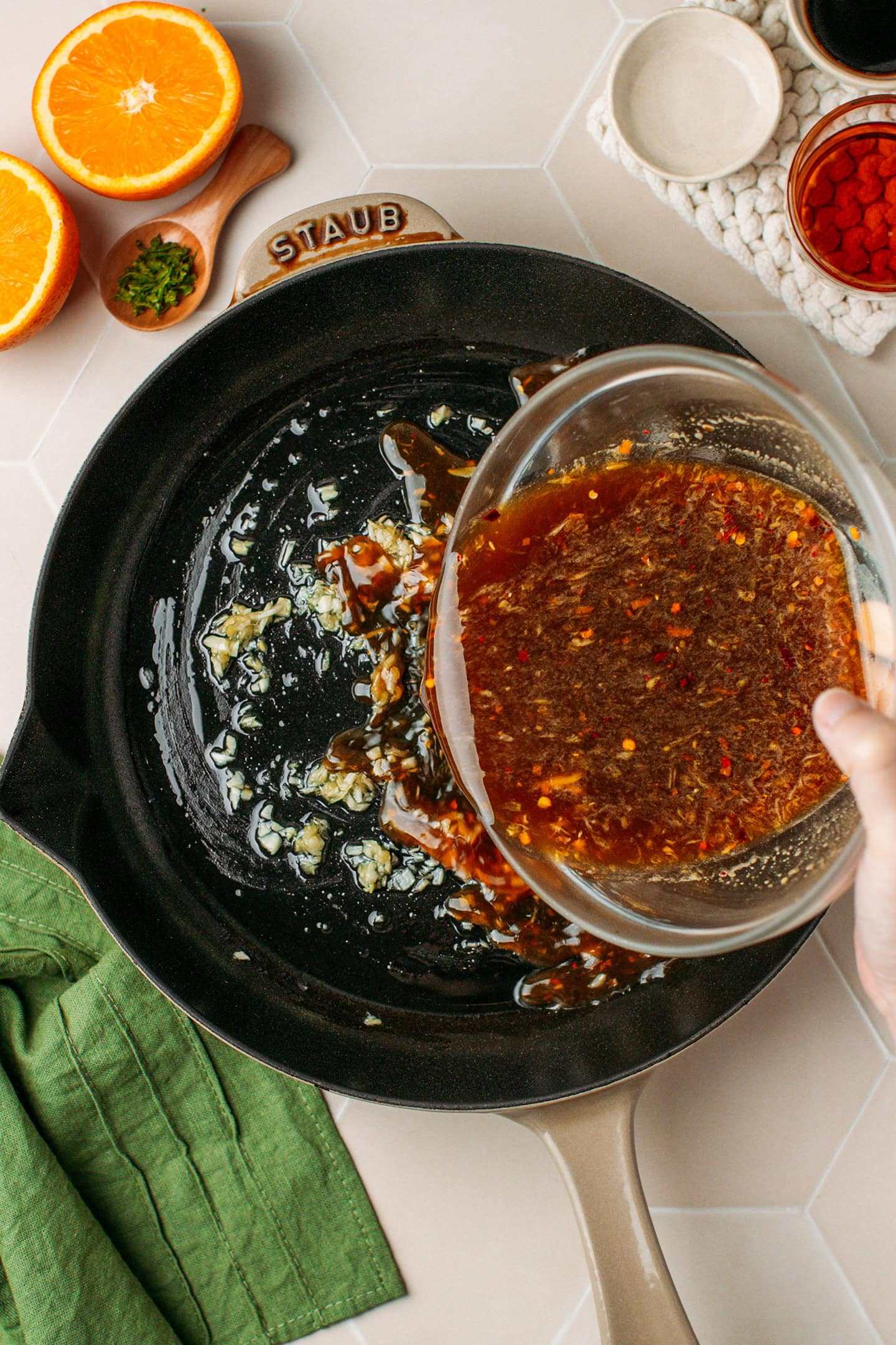 Pouring orange sauce into a skillet.