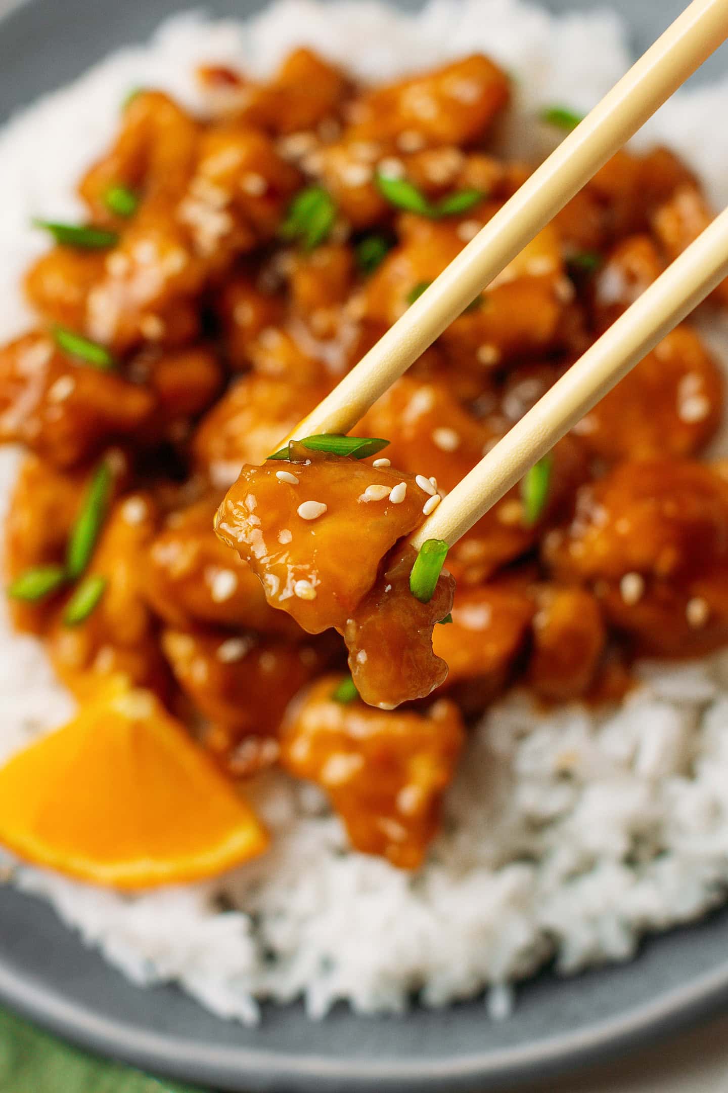Close-up of a pair of chopsticks holding a piece of orange tofu.
