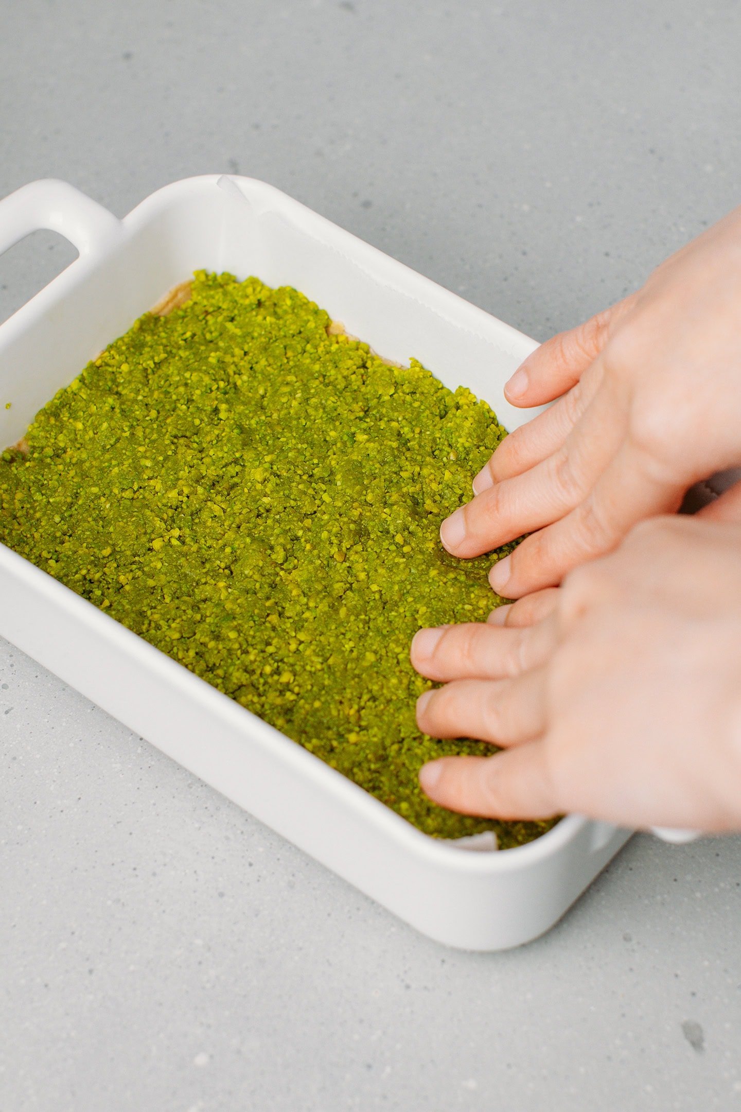 Pressing pistachio meal over a layer of shortbread inside a baking dish.