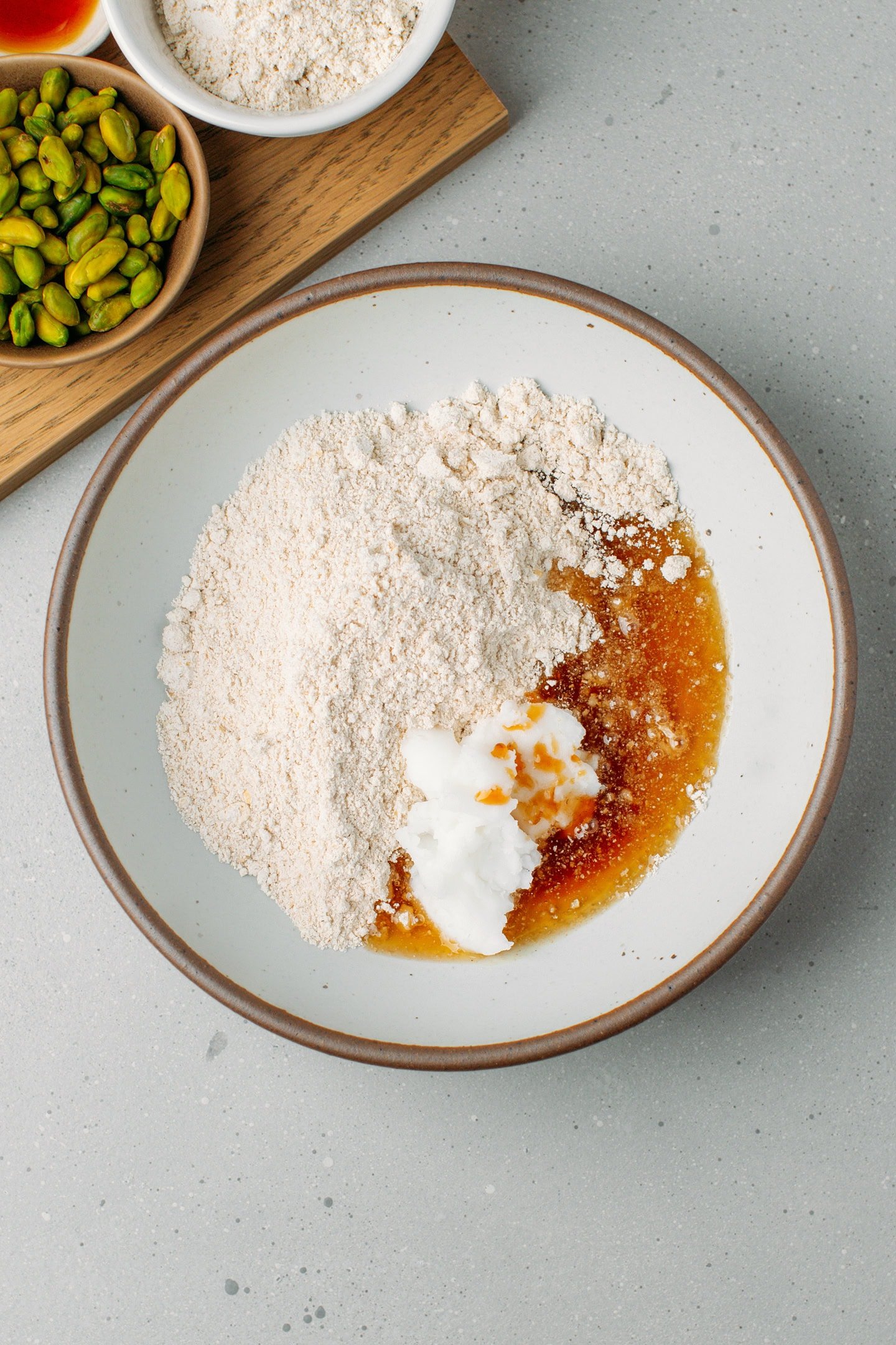 Oat flour, coconut oil, maple syrup, and vanilla extract in a bowl.