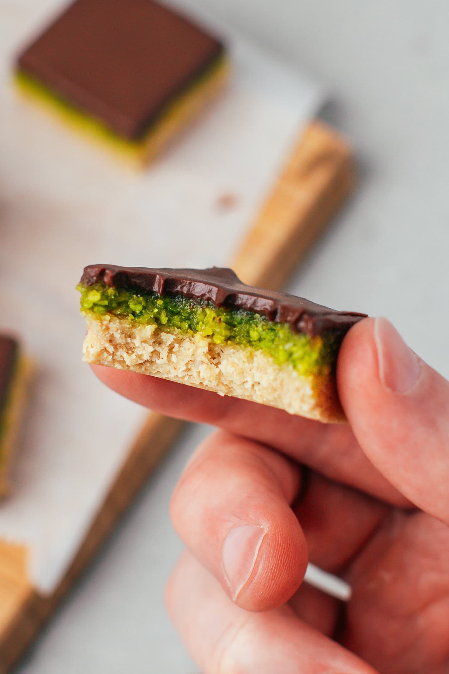 Holding a chocolate pistachio bar with a bite mark.