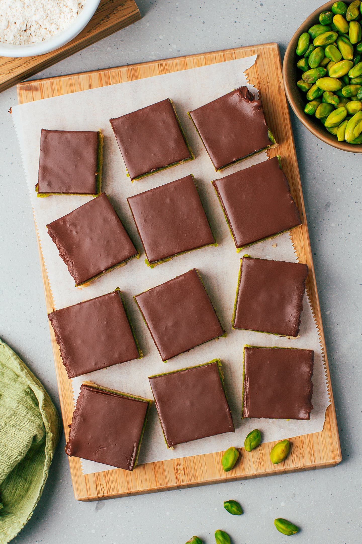 Twelve squares of no-bake pistachio bars on a wooden board.