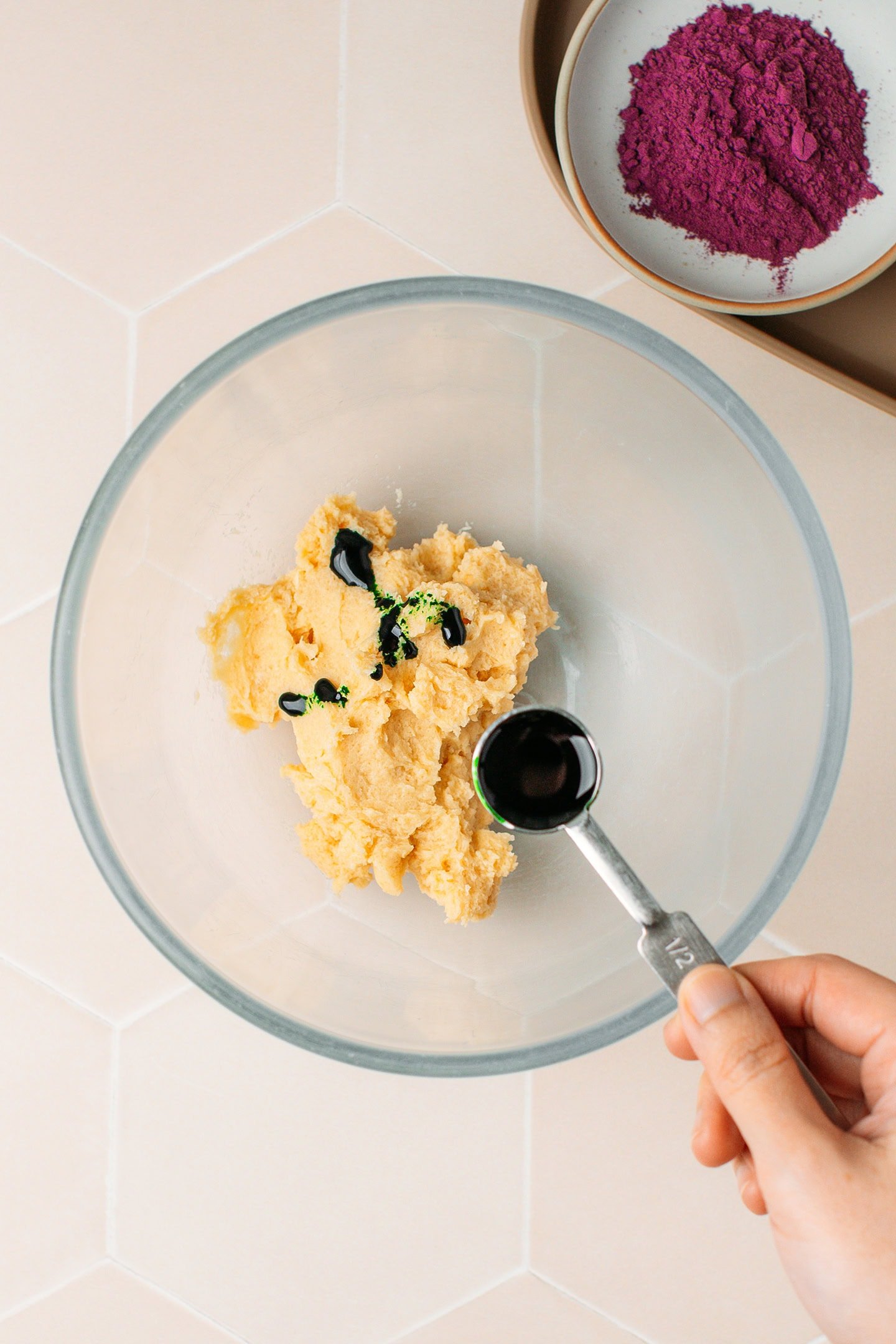 Adding pandan extract to a bowl containing creamed butter.