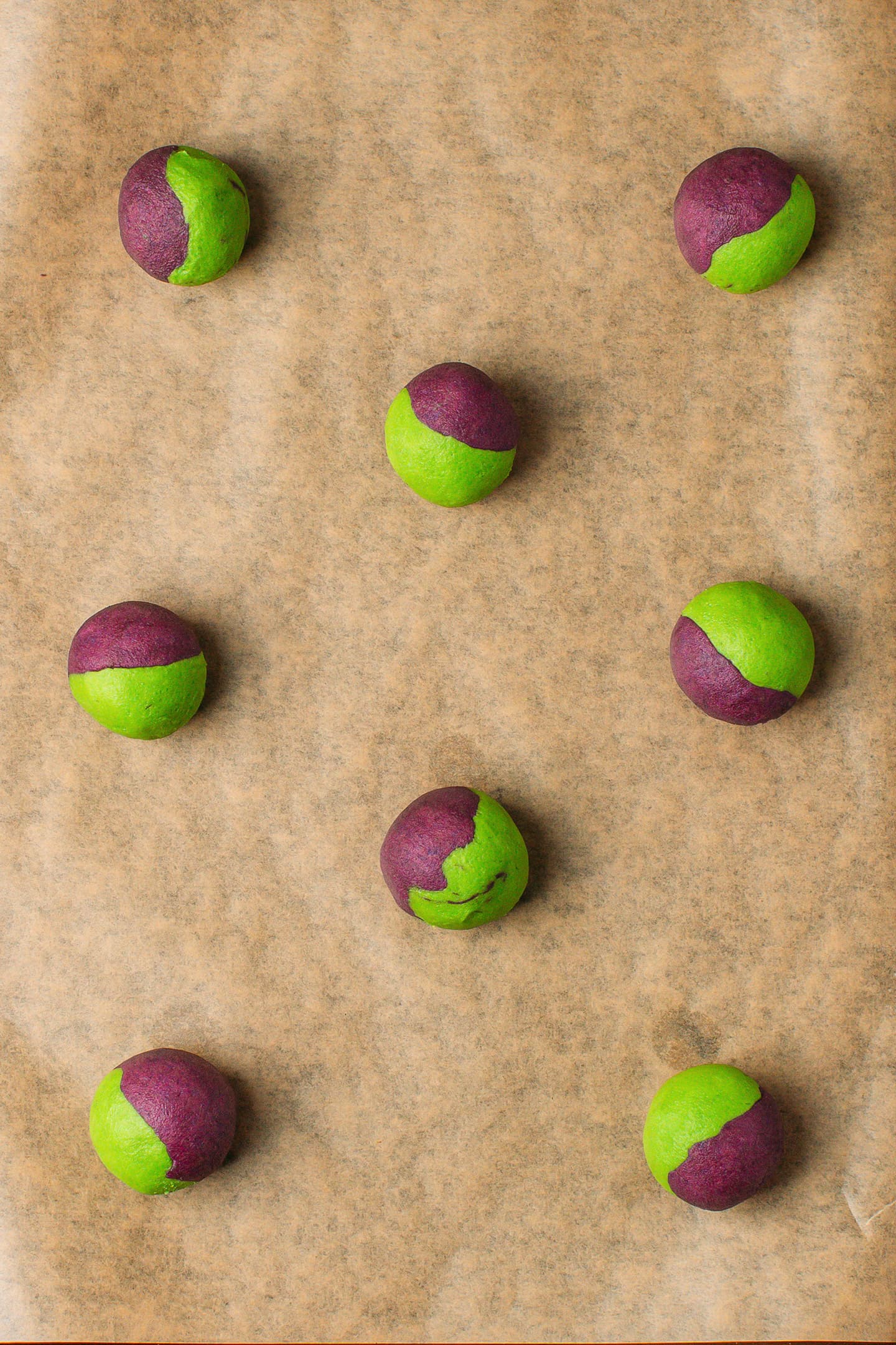 Ube and pandan cookie dough balls on a baking sheet.