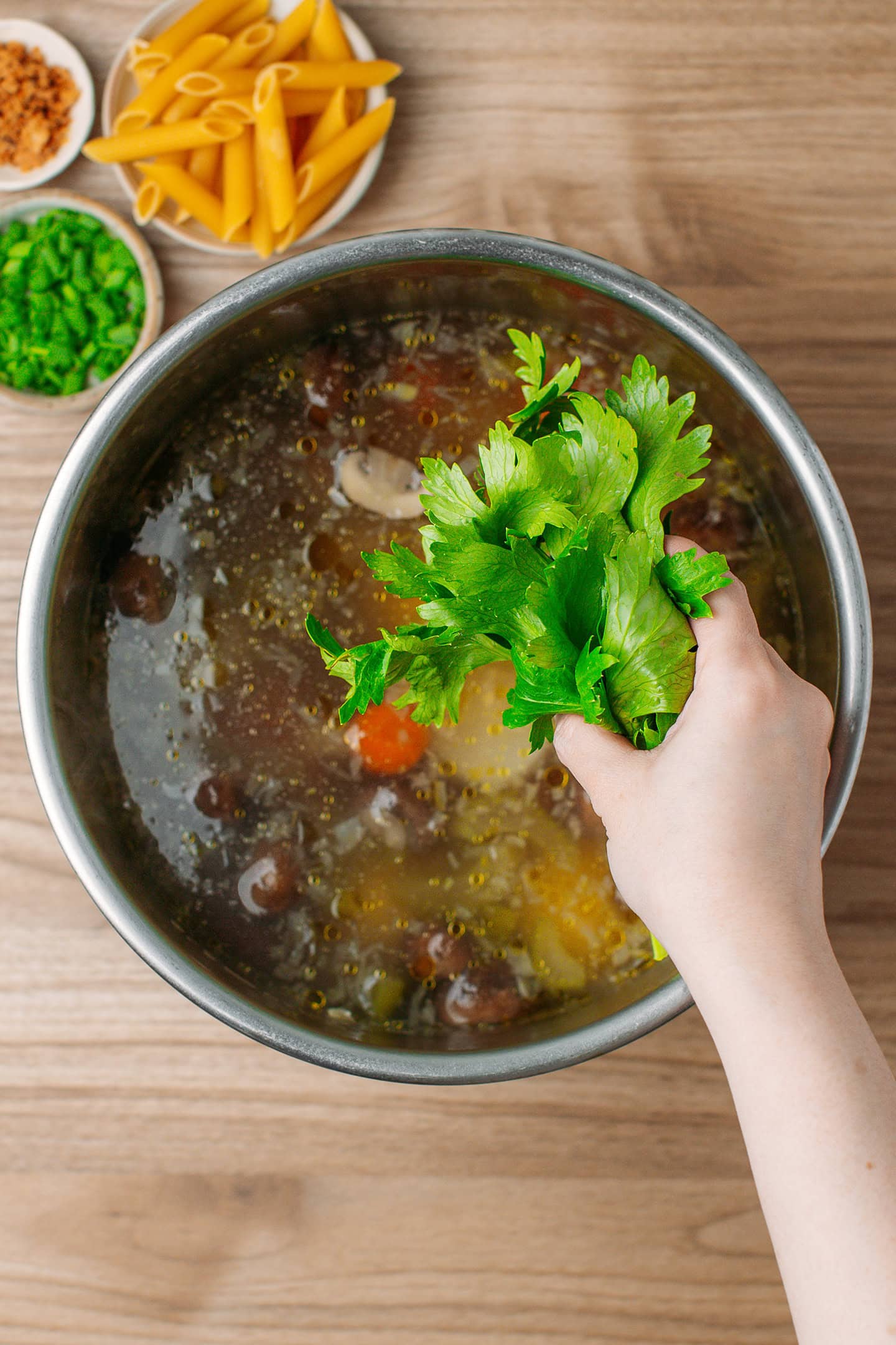 Adding celery leaves to a pot of vegetable soup.