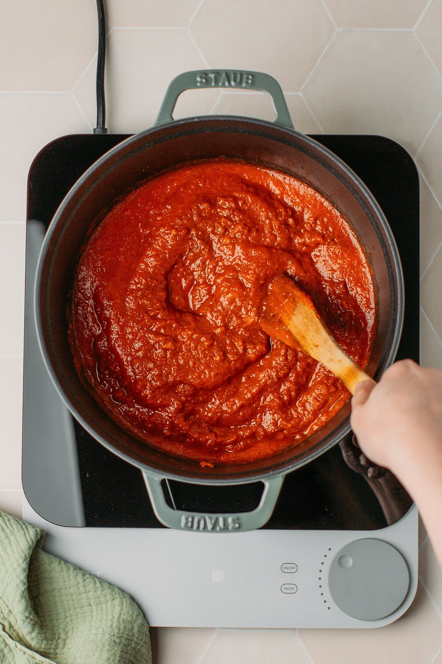 Stirring tomato sauce with spices in a deep pot.