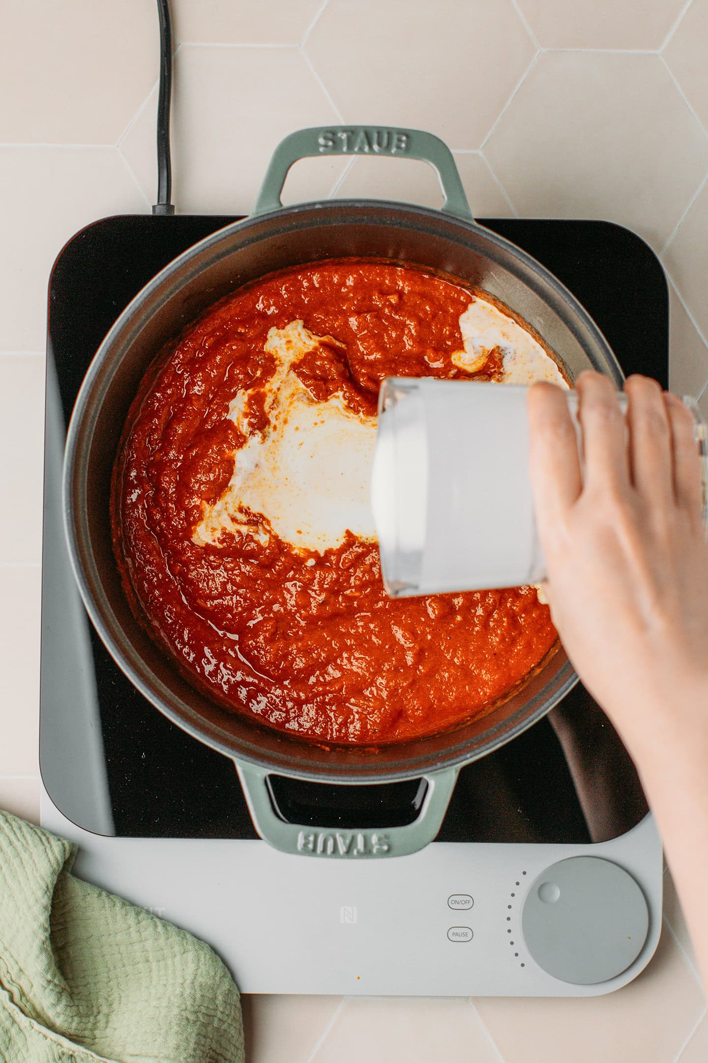Pouring coconut milk into a pot containing tomato sauce.