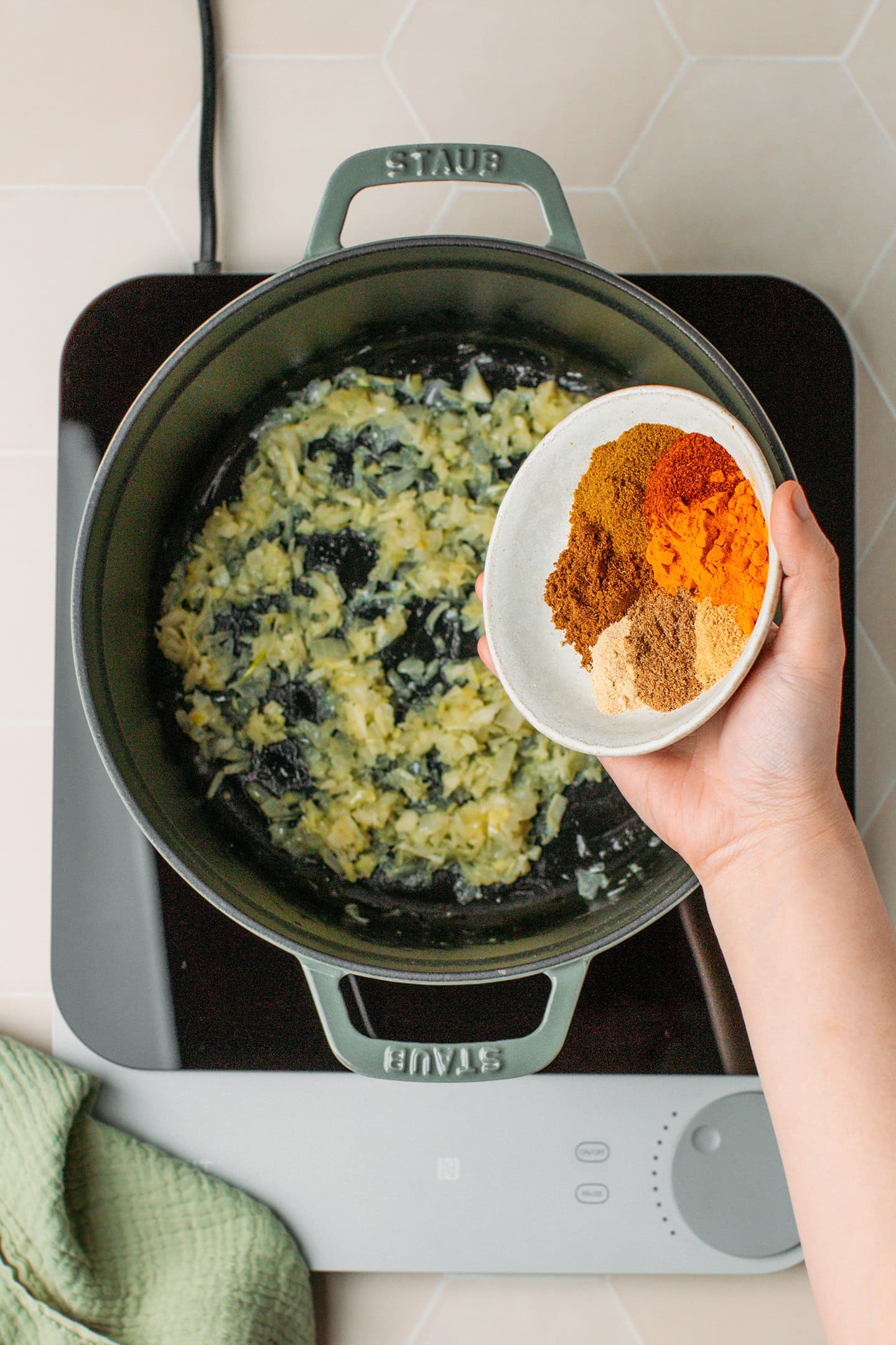 Adding spices to a pot containing saut&eacute;ed onions and garlic.