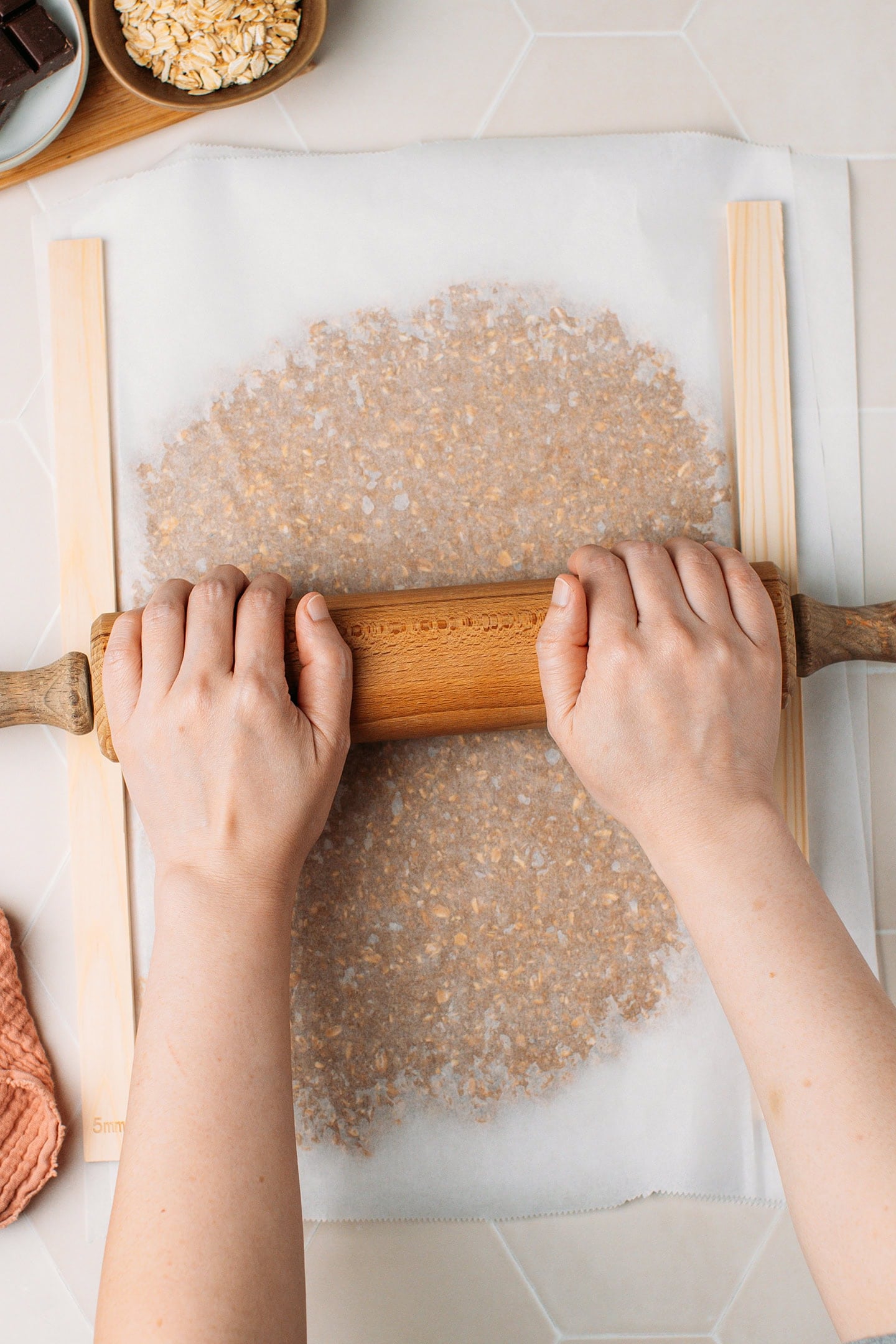 Flattening a granola mixture between two sheets of parchment paper.