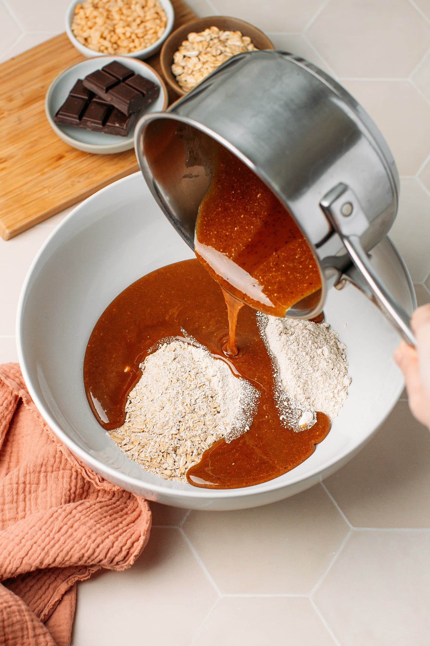 Pouring melted brown rice syrup and almond butter into a bowl containing oats.