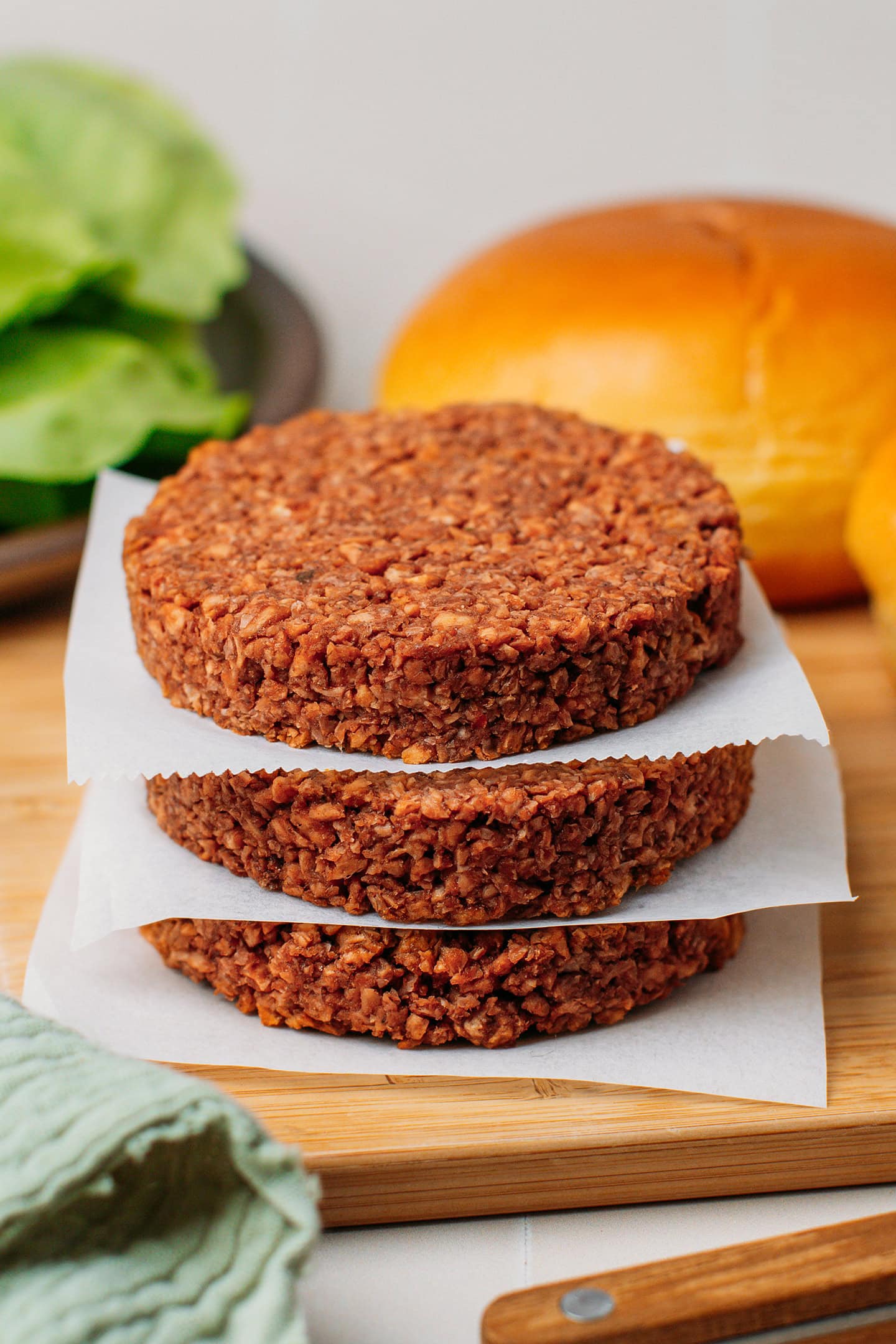 Three uncooked vegan patties stacked together on a wooden board.