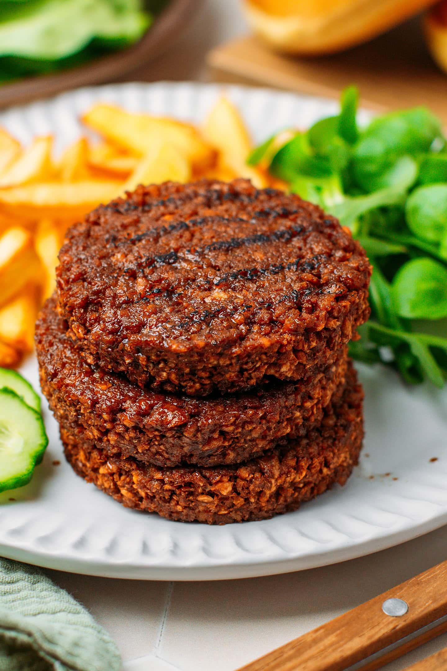 Three stacked vegan burger patties on a plate with French fries and salad.
