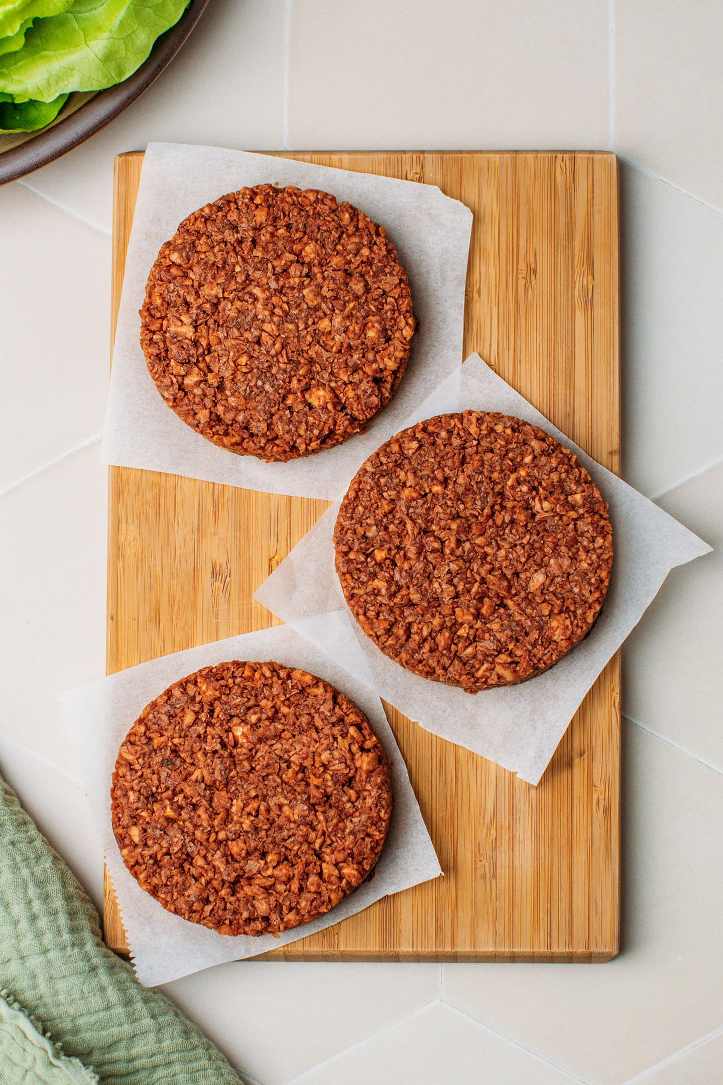 Three vegan meat patties on a cutting board.