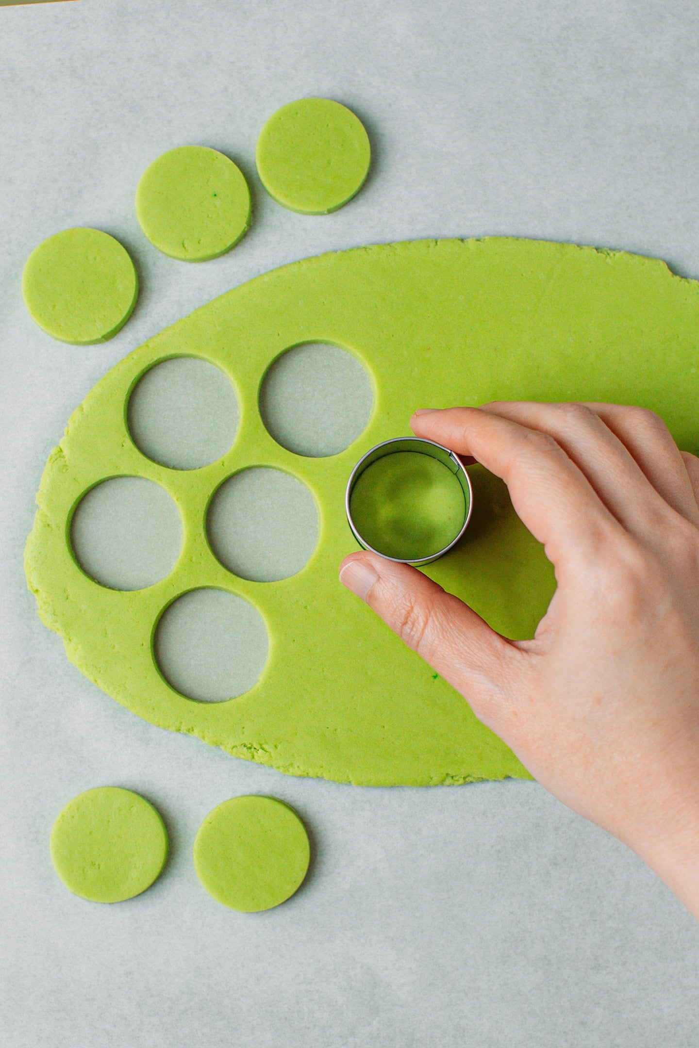 Using a round cookie cutter to cut out dots in a green dough.