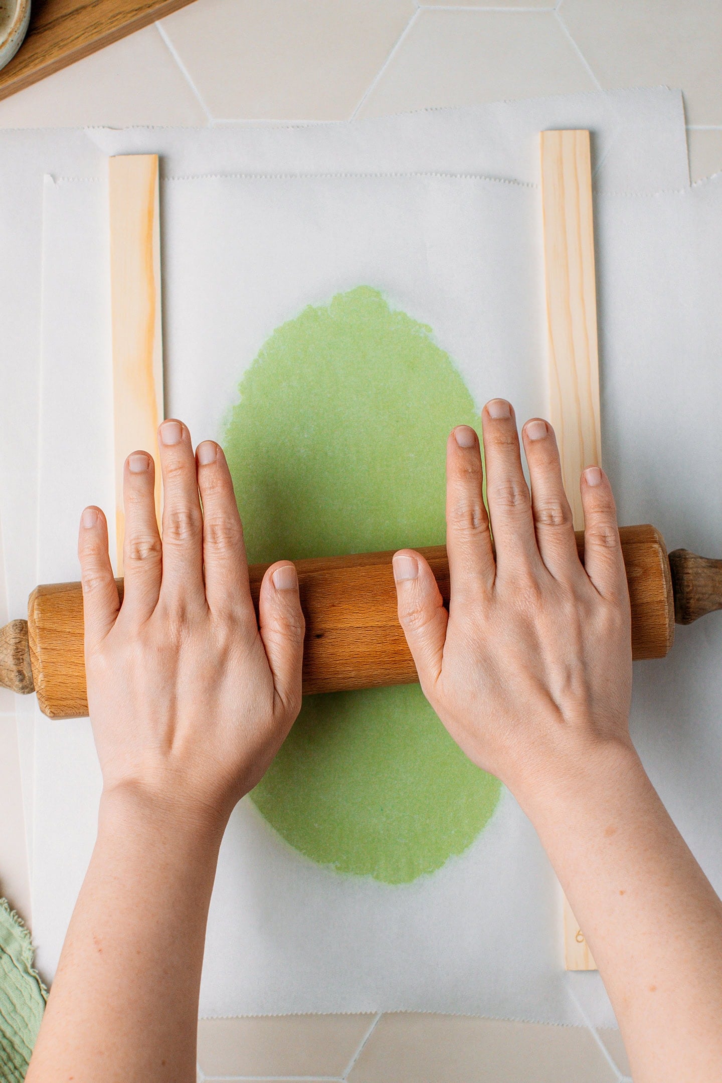 Using a rolling pin to flatten green cookie dough.