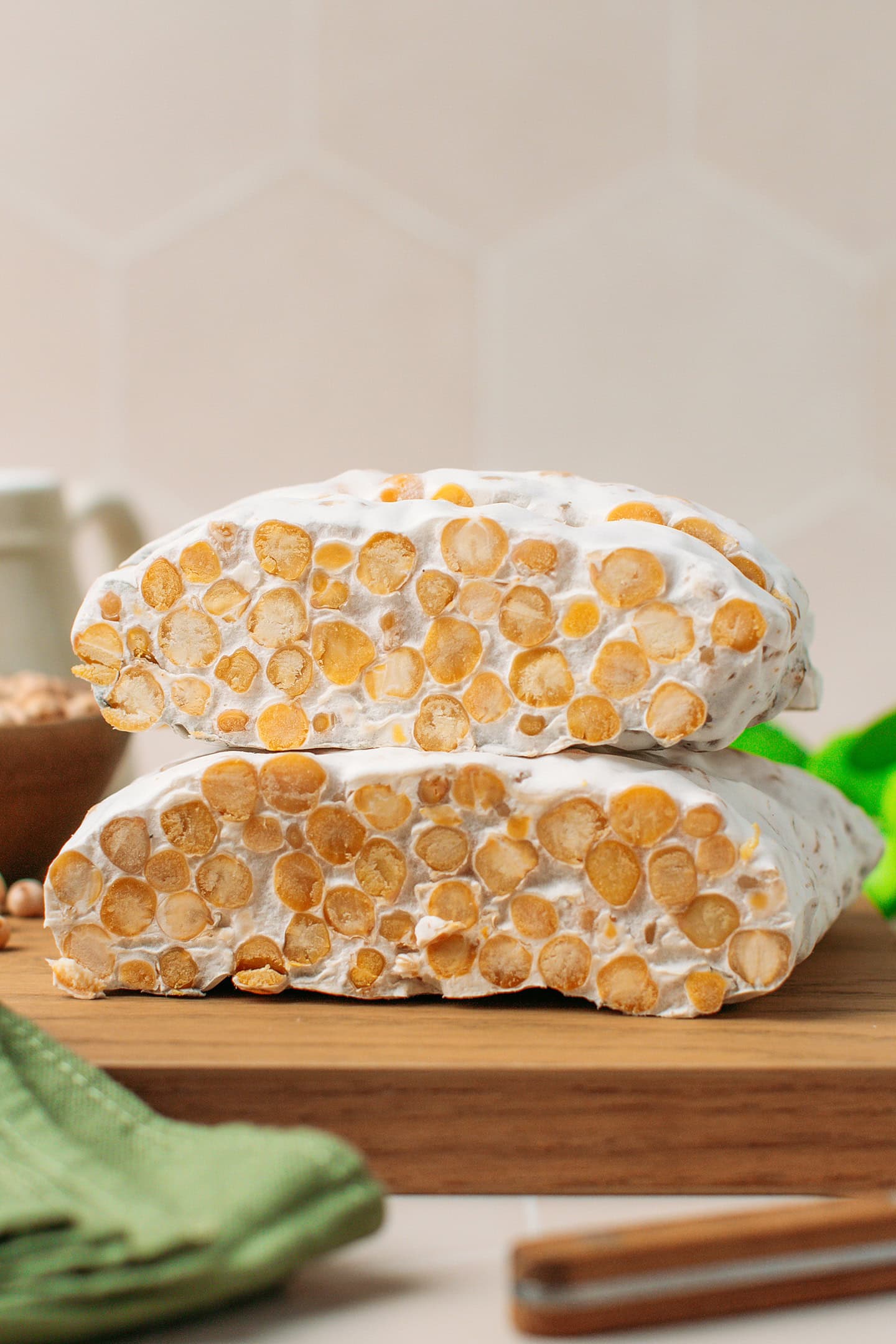 Two loaves of chickpea tempeh stacked on a wooden board.