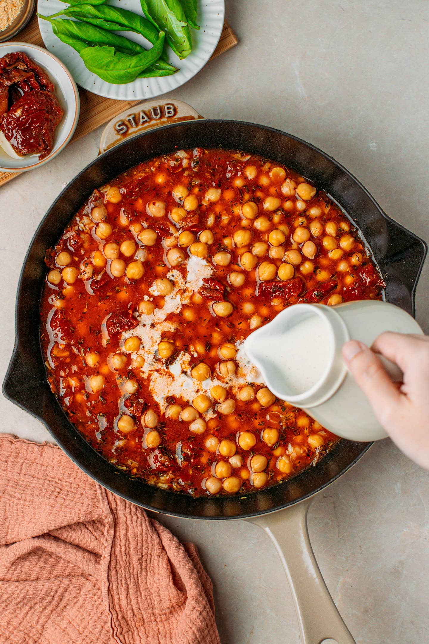 Pouring vegan cream into a skillet containing vegetable broth and cooked chickpeas.