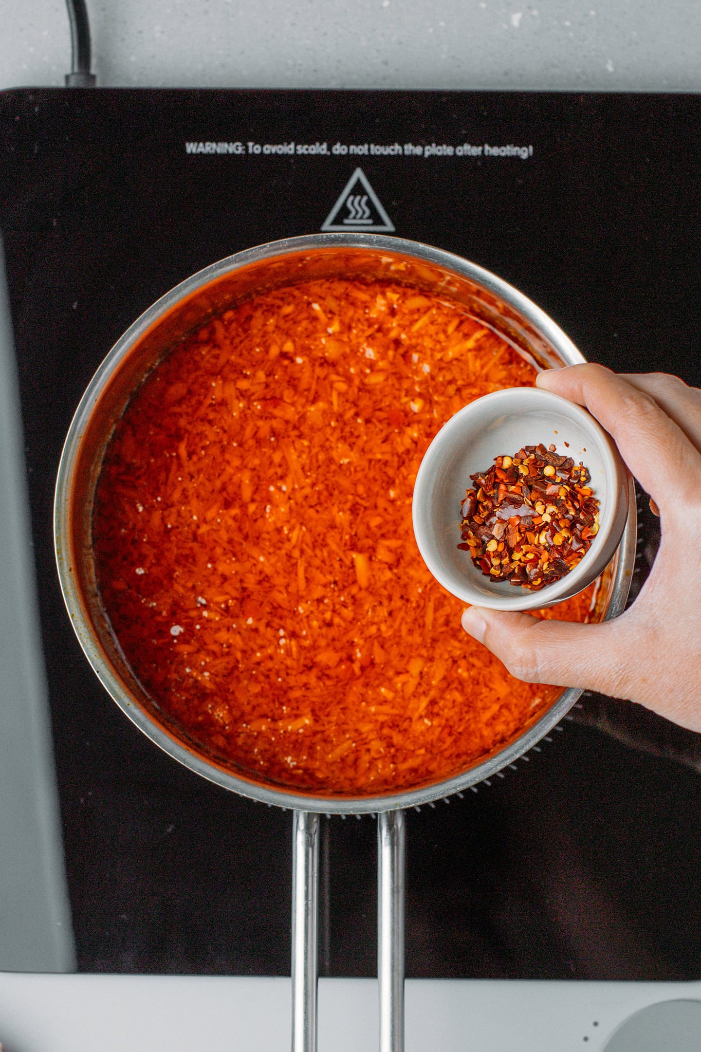 Adding chili flakes to chili oil in a saucepan.
