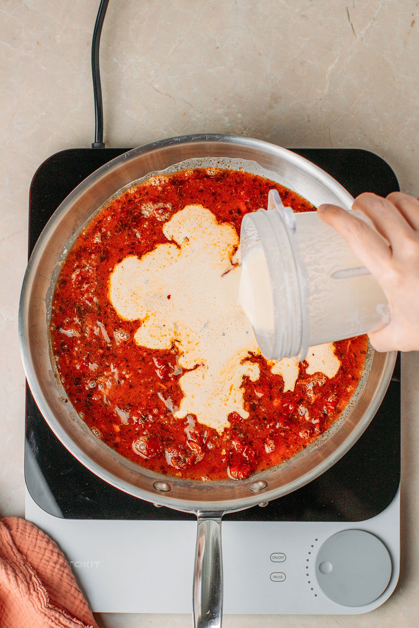 Pouring cashew cream in a skillet containing a sun-dried tomato sauce.