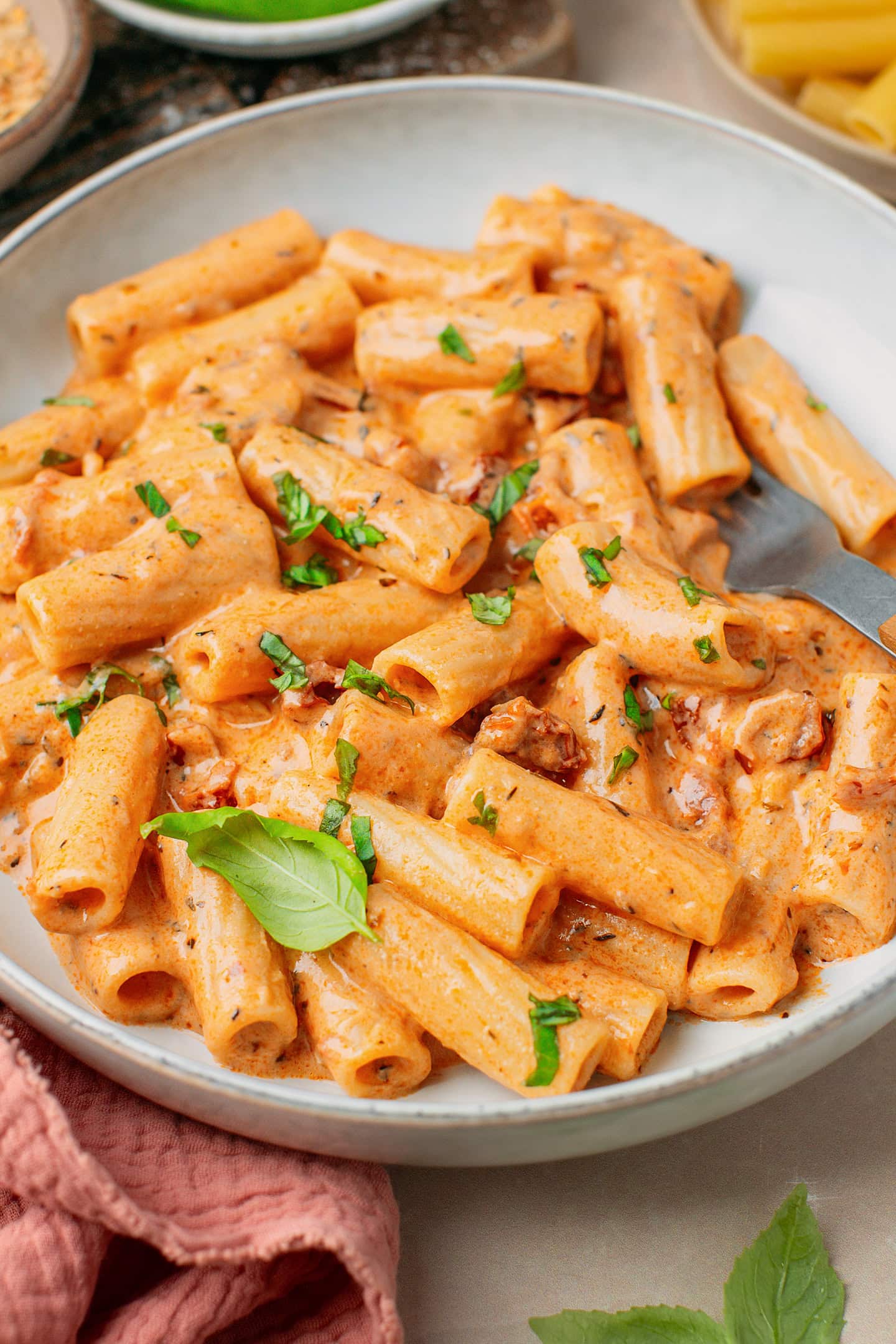 Close-up of pasta coated with a creamy sun-dried tomato sauce inside a deep plate.