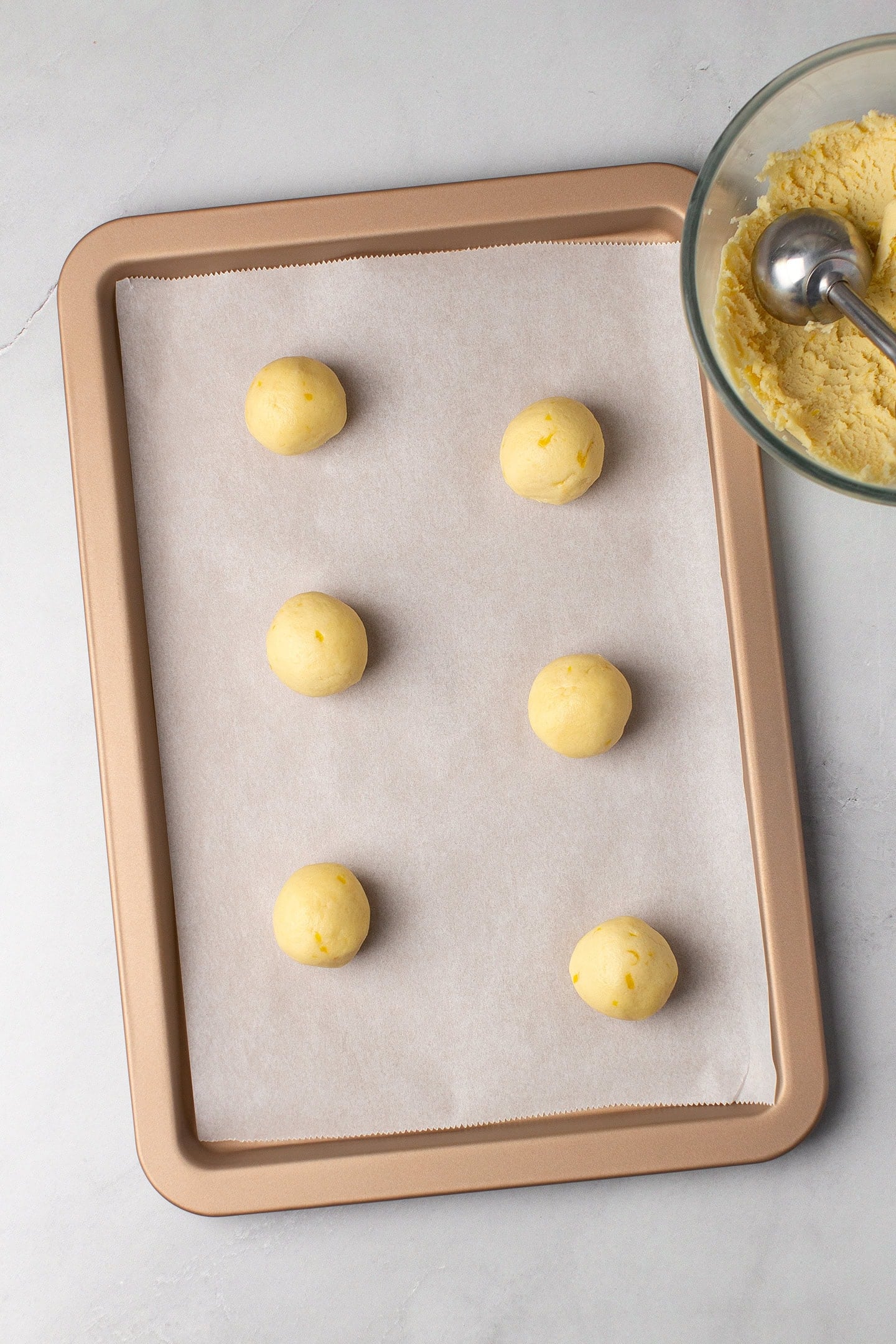 Six lemon cookie balls on a baking sheet.