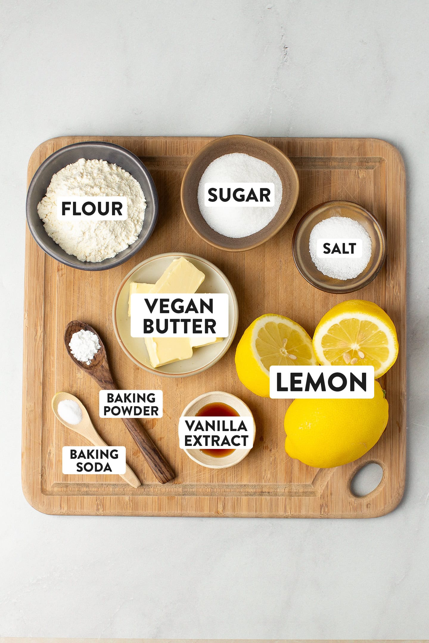 Ingredients like lemons, flour, sugar, vegan butter, baking powder, and vanilla extract.