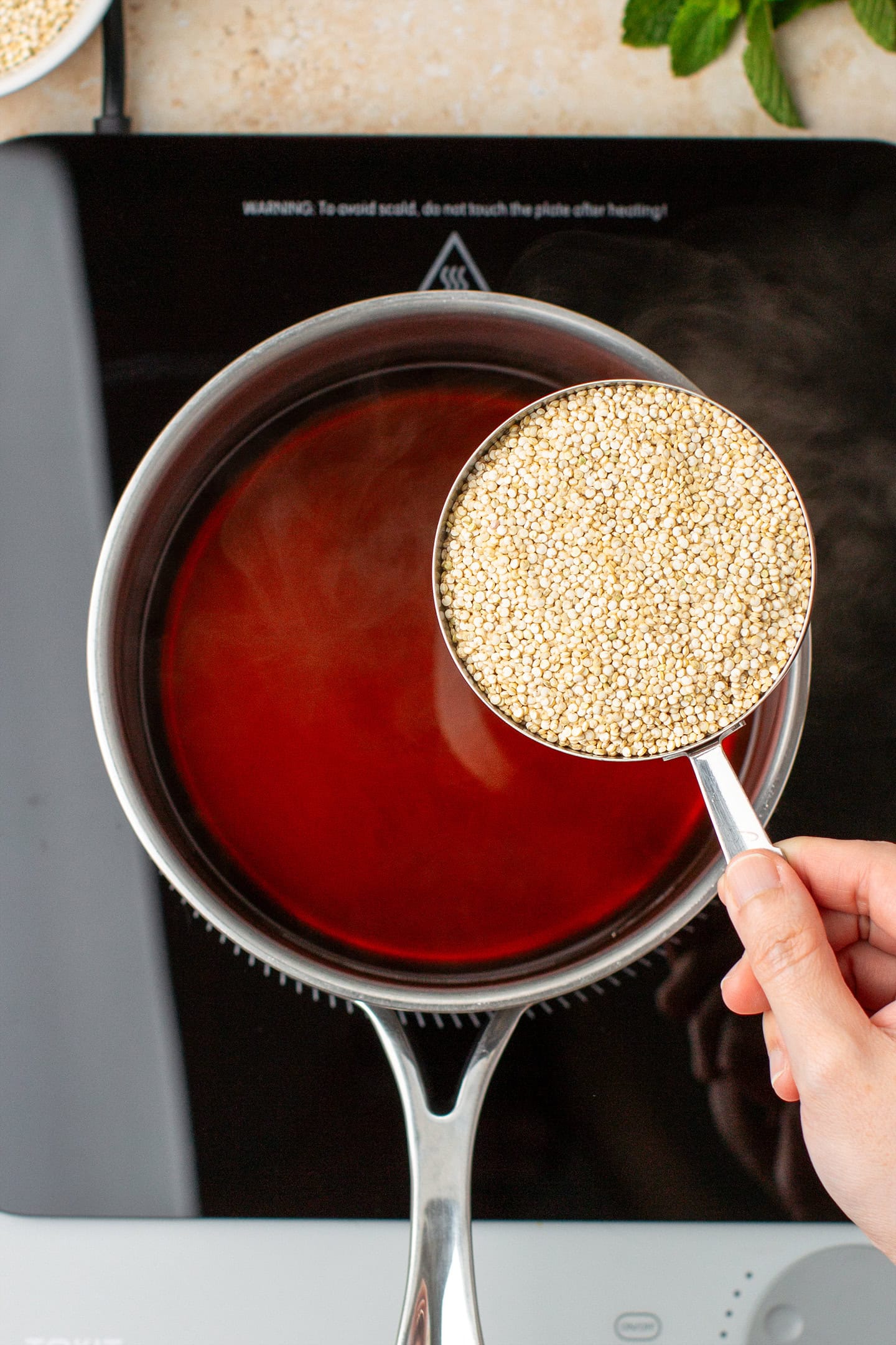 Holding a cup of dry quinoa over a pot of boiling water.