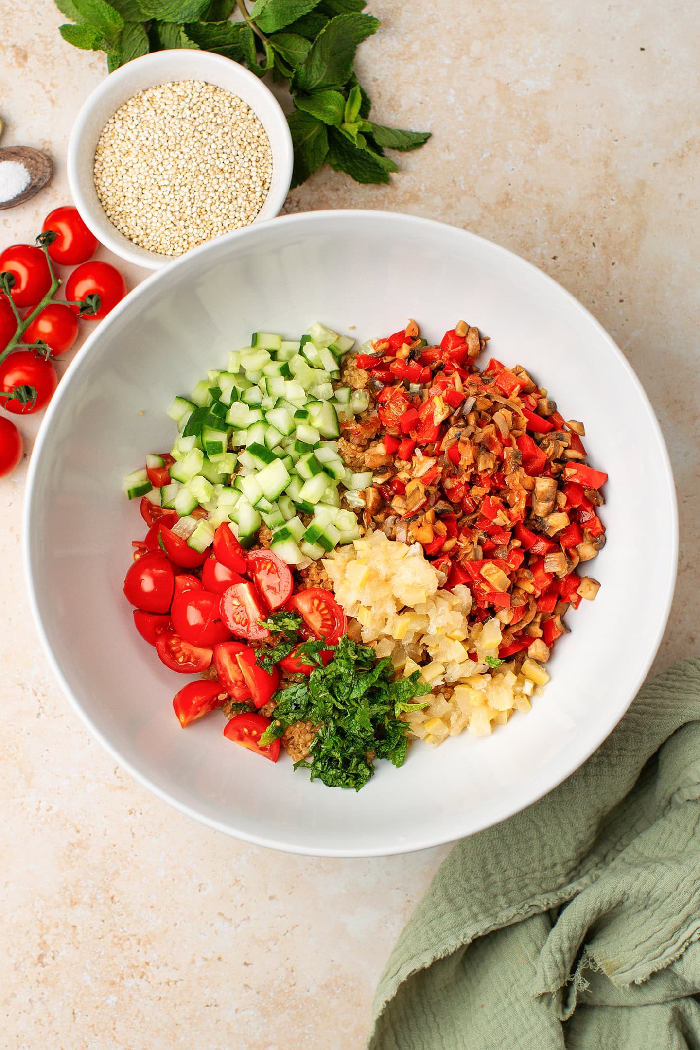 Large bowl filled with quinoa, diced cucumber, chopped preserved lemon, mint, and cherry tomatoes.