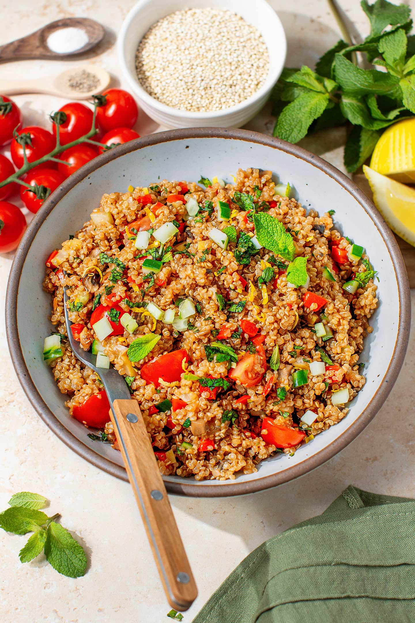 Fresh quinoa salad with diced cucumber, cherry tomatoes, lemon, and mint leaves.