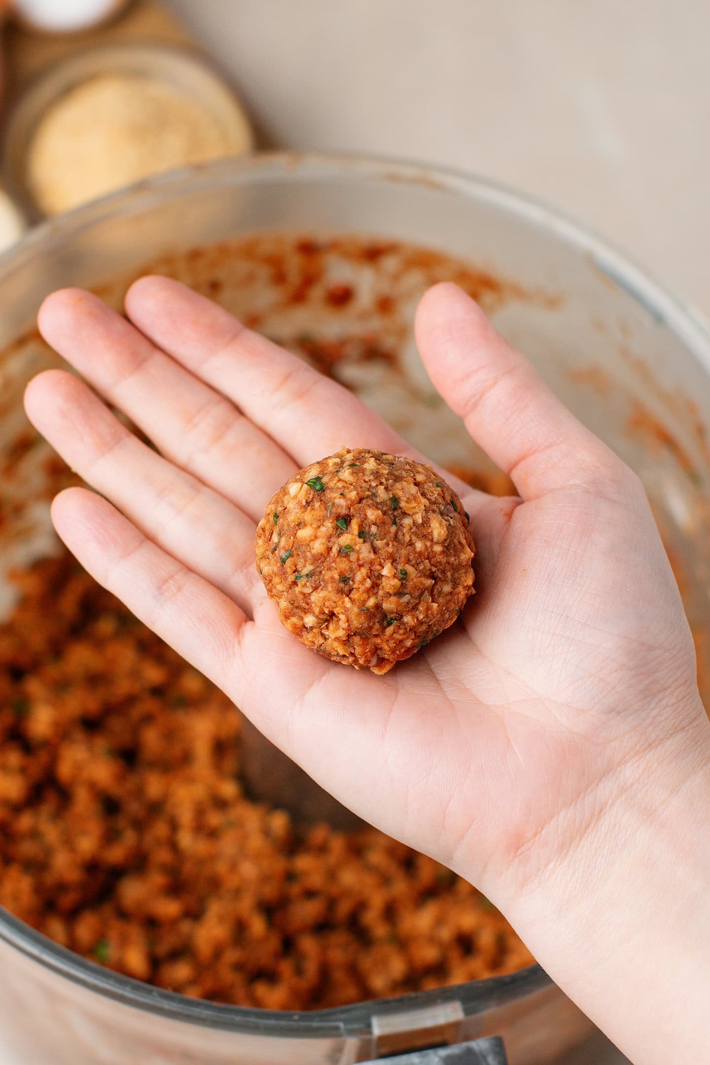 Holding an uncooked vegan meatballs.
