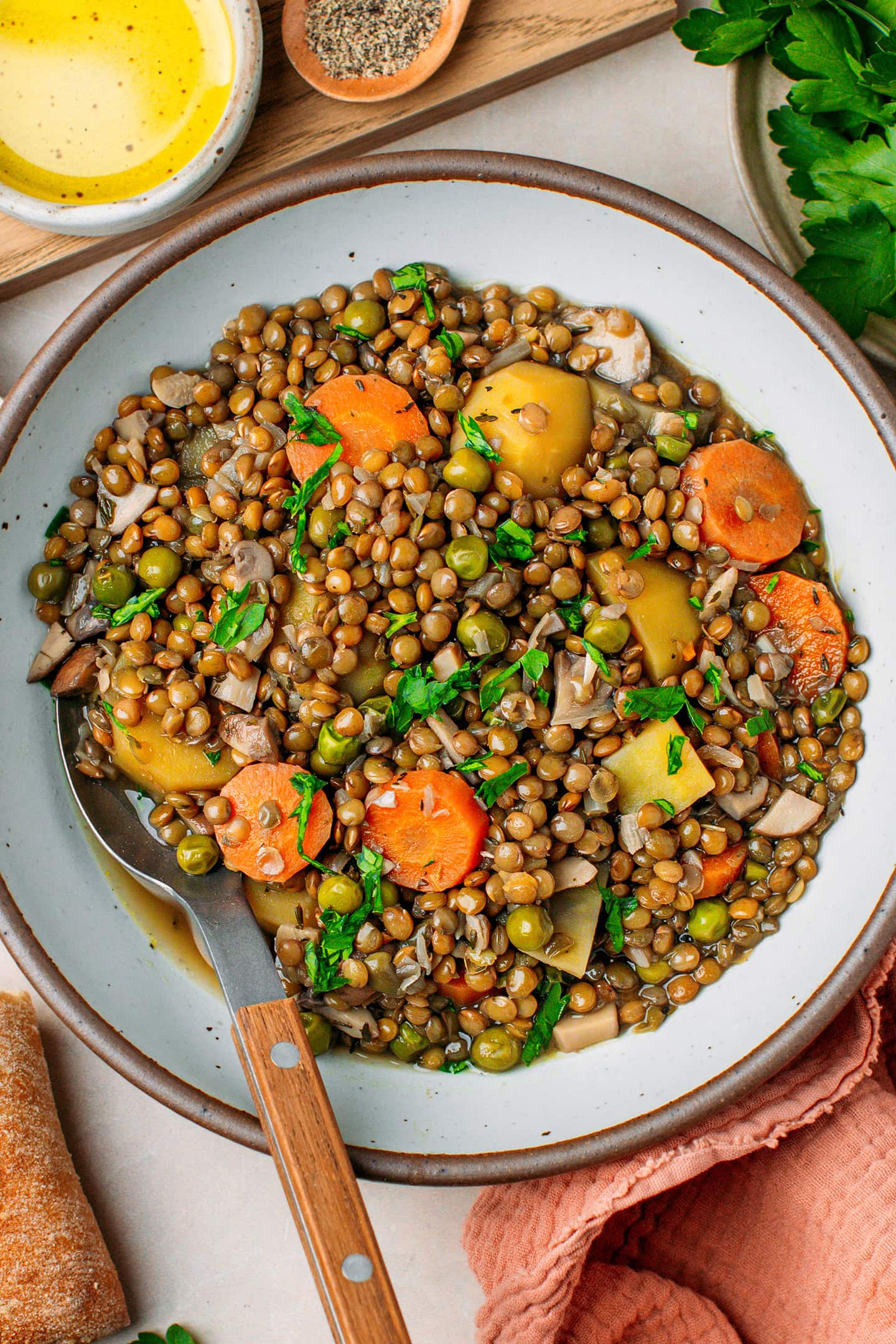 Bowl filled with cooked green lentils, potatoes, green peas, and carrots.